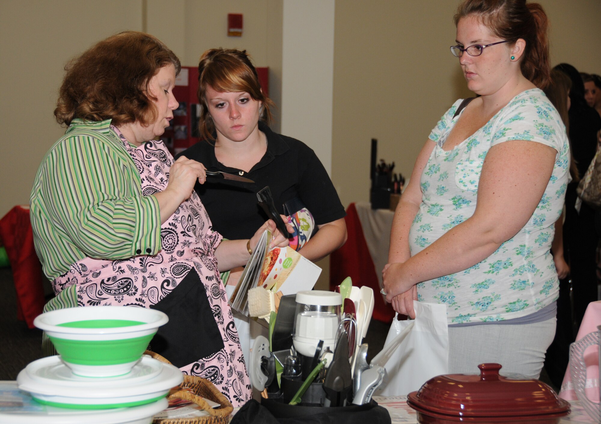 Joy Domin, left, from Pampered Chef shows some products to Fawn Lipe and Caitlin Wildes during Pamper Me Day, May 7 at the Roberts Consolidated Aircraft Maintenance Facility.  Spouses are Airmen 1st Class Casey Lipe and Christopher Wildes, students in the 338th Training Squadron.  The annual event sponsored by the airman and family readiness center featured agencies, vendors, giveaways, activities, business and product displays and information booths.  (U.S. Air Force photo by Kemberly Groue)