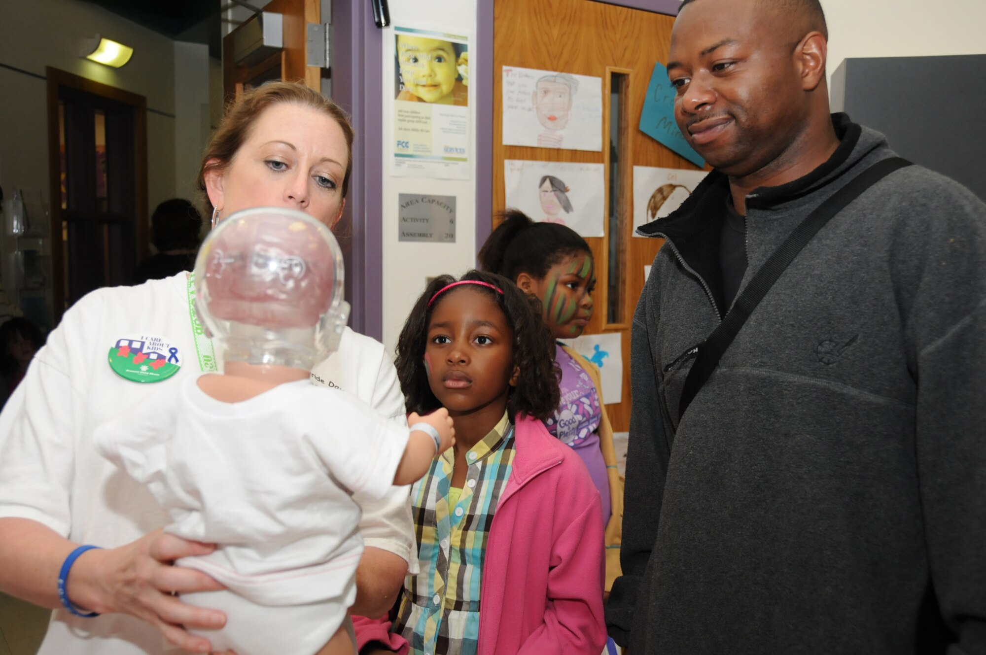Ms. Tracy demonstrates the simulator doll to Dionna Samuel, 8, and her dad, Tech. Sgt. Darnell Samuel, 81st Training Support Squadron, during Child Pride Day, April 24.  (U.S. Air Force photo by Kemberly Groue)