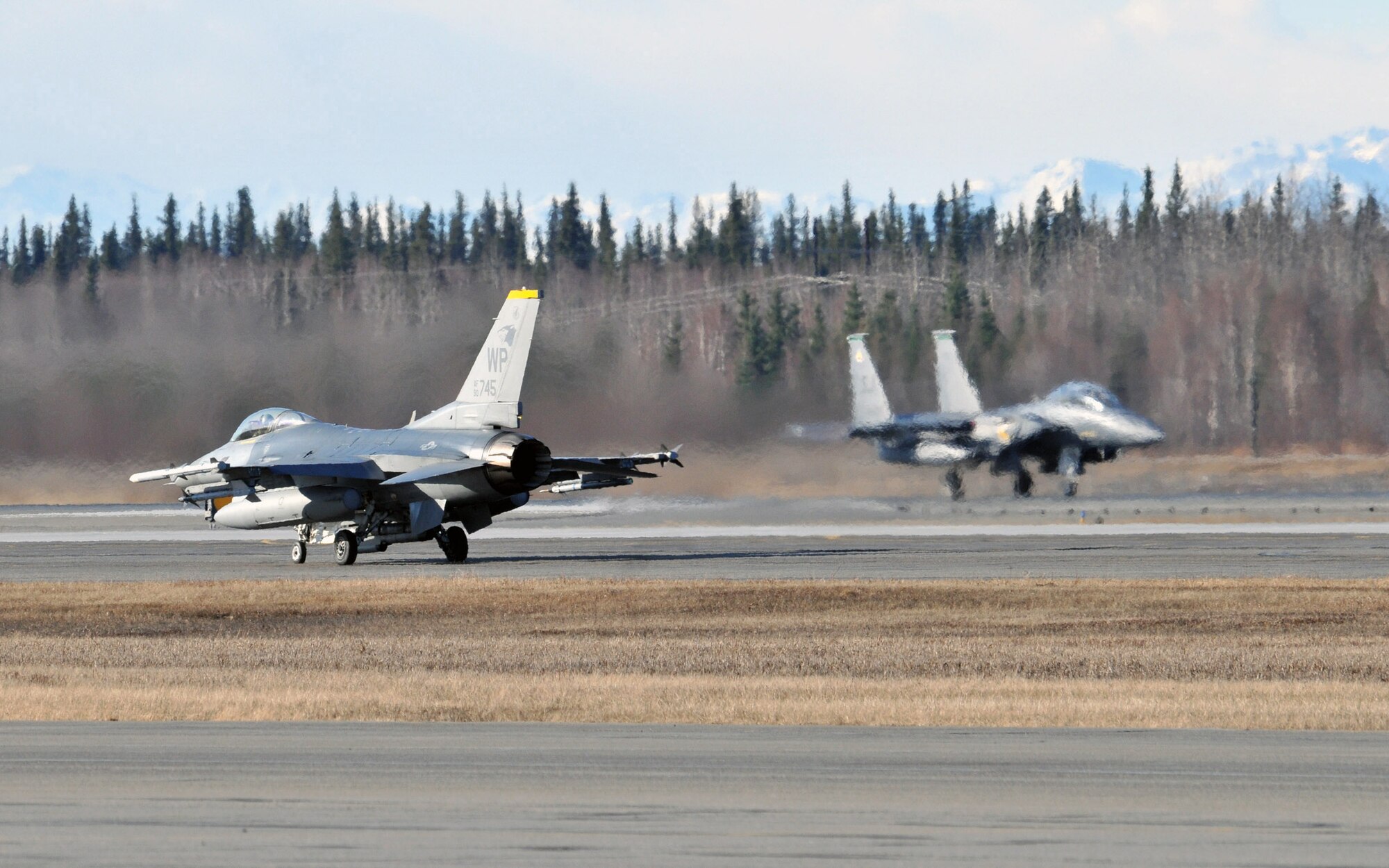 1st Lt. Jondavid Hertzel, 80th Fighter Squadron Headhunters F-16 Fighting Falcon pilot, taxis to the end of runway as an F-15E Strike Eagle from Seymour Johnson Air Force Base, N.C., takes off during Red Flag-Alaska at Eielson Air Force Base, Alaska, April 21. Lieutenant Hertzel is deployed from the 8th Fighter Wing, Kunsan Air Base, Republic of Korea. (U.S. Air Force photo/Capt. Shannon Collins)