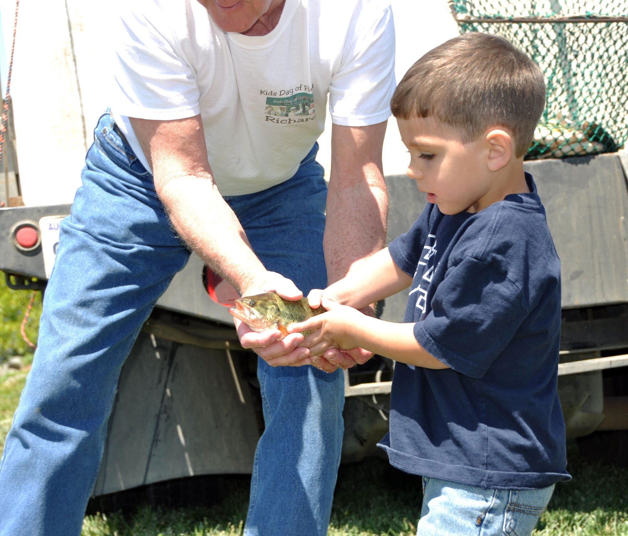 An employee of the Lazy Q Fishing Company helps Noah Snyder prepare to release a fish into the Duck Pond May 6. Approximately 800 bass were released into the pond in preparation for the Kids Day of Fishing event that took place May 8. (U.S. Air Force photo/Senior Airman Kristen Rohrer)  