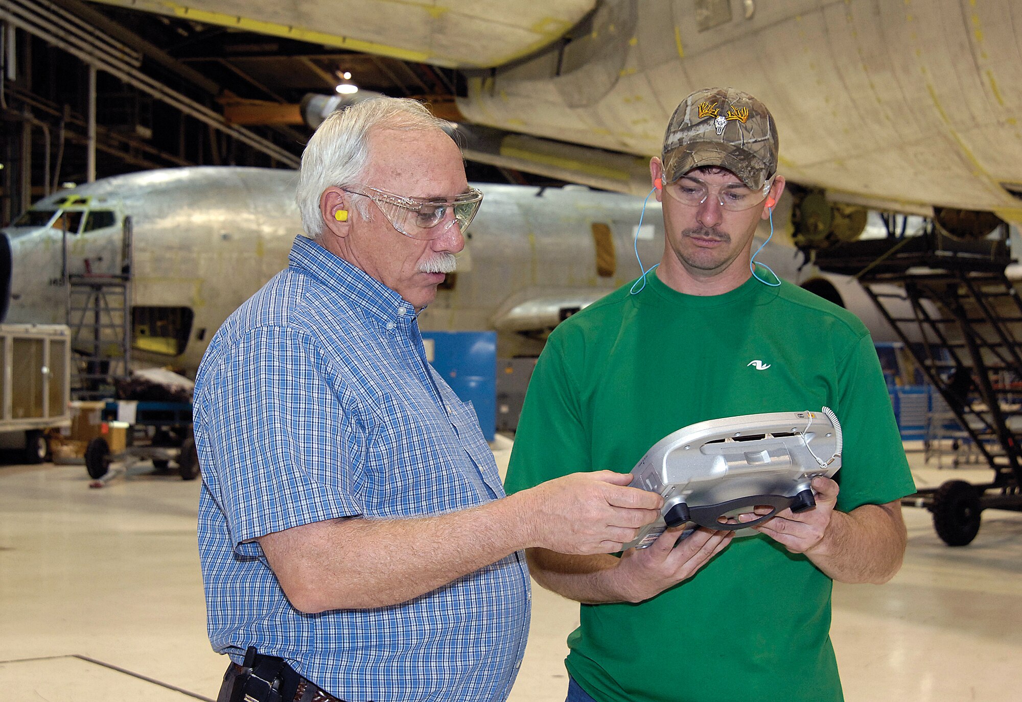 Dan Crowe, left, a 72nd Air Base Wing Communications Directorate computer specialist, talks with KC-135 aircraft mechanic Bill McGraw about a hand-held rugged computer that many hope will bring further efficiency to the workers planeside.  Tough enough to withstand bumps and falls, the wireless handheld can pack in hundreds of technical orders that can be updated quickly, and can take photos of anything a mechanic finds during work that needs to be seen quickly by others such as engineers. (Air Force photo by Margo Wright)