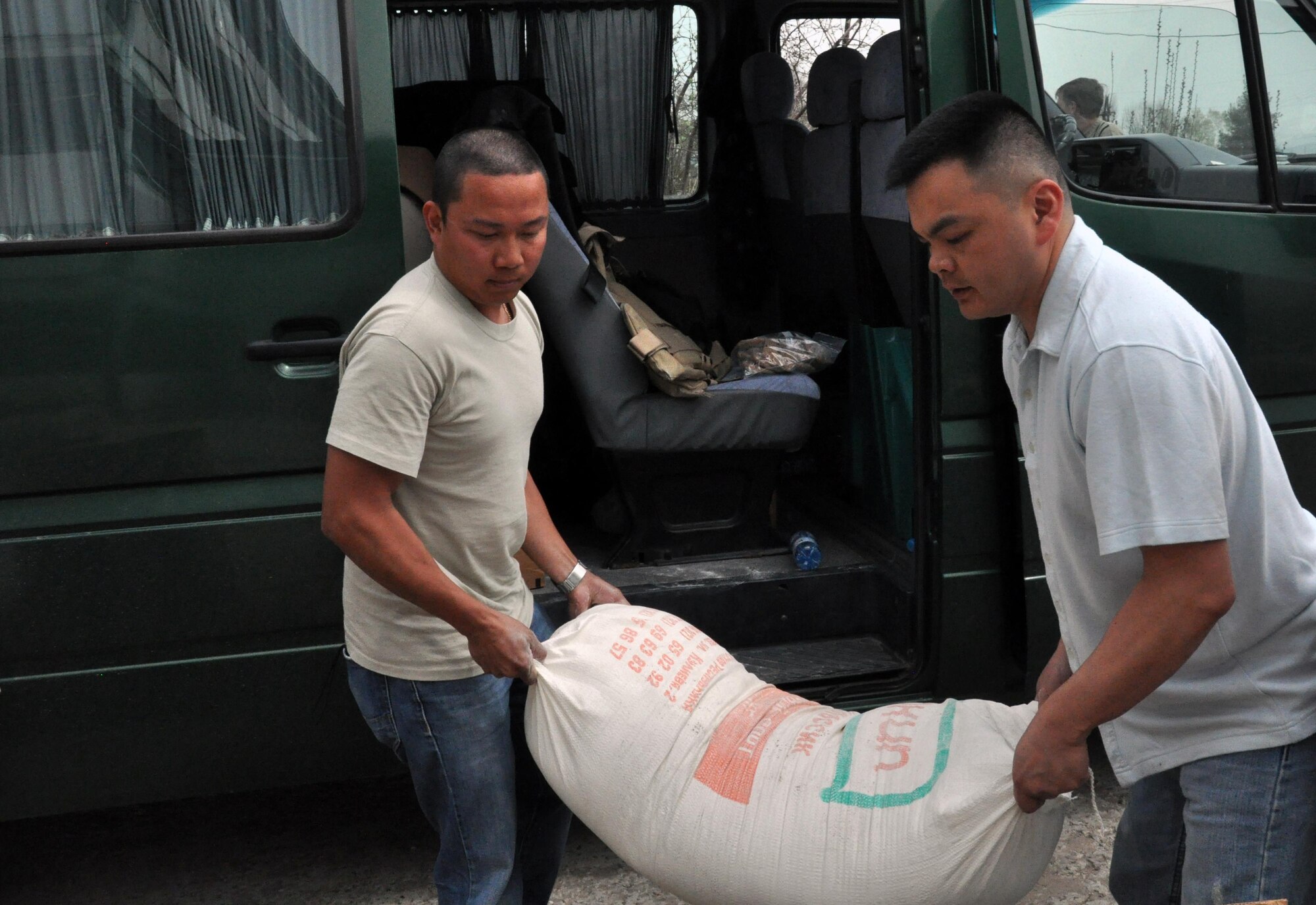 U.S. Air Force Staff Sgt. Jeff Legaspi carries a 100-pound bag of flour for the residents of the TokMok Psychoneurologic Boarding House with Capt. Tom Mulka April 14, 2010, in Iskra Village, Kyrgyzstan. Sergeant Legaspi is a 376th Expeditionary Civil Engineer Squadron electrical engineer deployed to the Transit Center at Manas, Kyrgyzstan. (U.S. Air Force photo/Staff Sgt. Carolyn Viss)