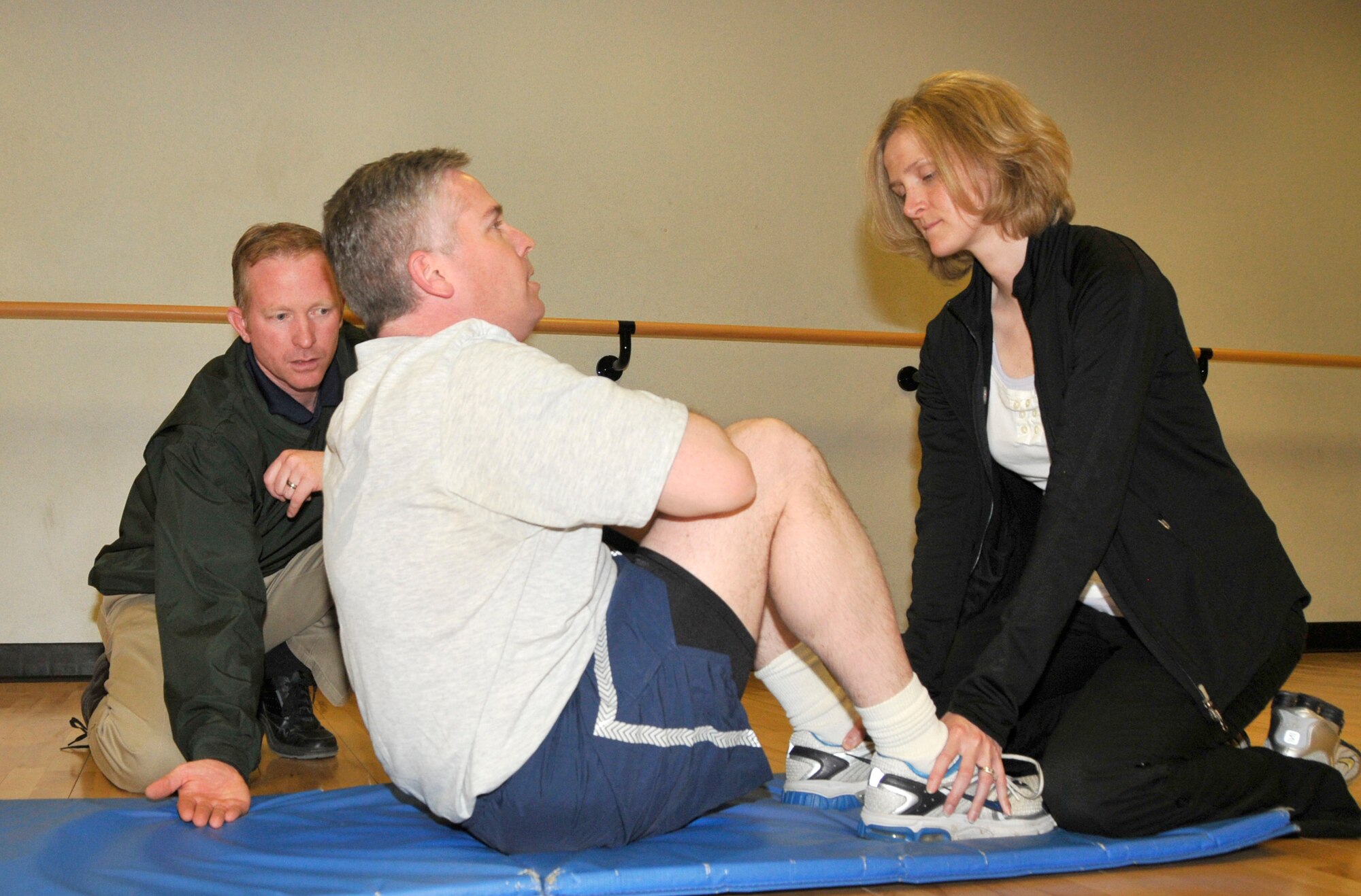 Rick Lyons, 48th Force Support Squadron lead fitness assessment cell, holds his hand at the bottom of the shoulder blade of Tech. Sgt. Christopher Campbell, 48th Fighter Wing Public Affairs NCO in-charge of internal operations,  while Jennifer Sibble, 48th Force Support Squadron fitness assessment cell, holds his feet. Sergeant Campbell does as many sit-ups as he can in one minute. AS of July 1, only FACs will administer PT testing, and the Air Force issued PT gear will be required. (U.S. Air Force photo/Airman 1st Class Eboni Knox)