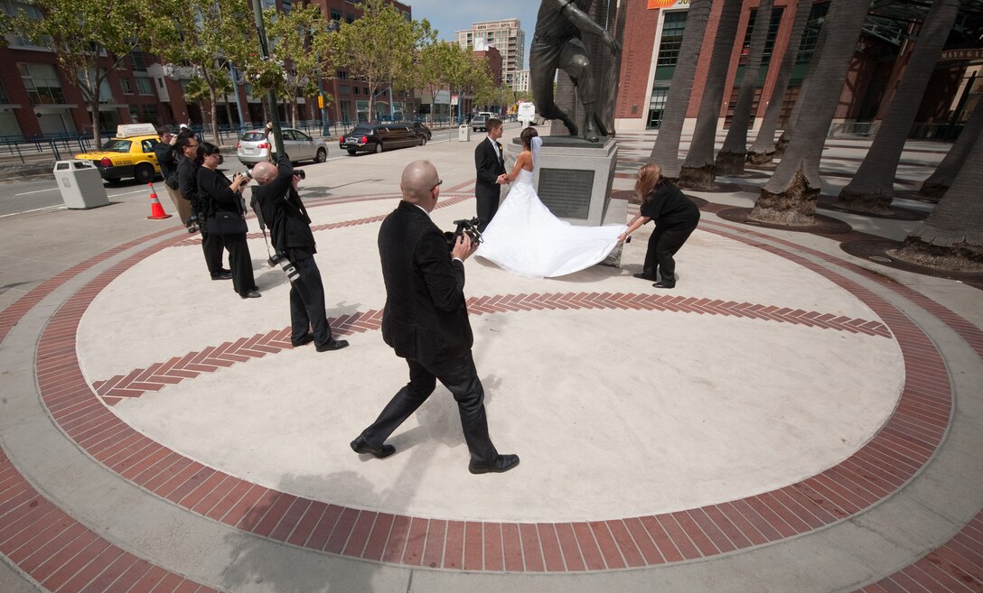 Vanessa Muza Teskey and Capt. Mike Hawkins (at statue) were brought to the AT&T Park baseball stadium for some of their wedding photos in San Francisco May 14, 2010. Amy Frugoli (right), wedding planner, makes some adjustments to the wedding dress before the multimedia team of James Burkart (left-right), Andrew Hsu, and Lilia and Raymond Ahner begin shooting at one of several photo locations. The wedding couple won the San Francisco Dream Wedding Giveaway with viewer votes. Mrs. Hawkins has been diagnosed with stage IV Hodgkin's lymphoma. Vendors donated $100,000 of goods and services to the couple's wedding day. (U.S. Air Force photo/Lance Cheung)