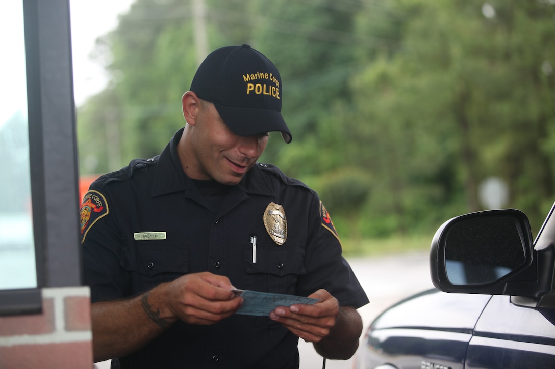 Tony Brienza, a patrol officer with first platoon, Provost Marshal’s Office, Marine Corps Base Camp Lejeune, checks a vehicle pass and a personal identification card at the main entry gate aboard the base, May 17.  Brienza is one of the Marine Corps Civilian Law Enforcement Program personnel with PMO who work with military police to protect service members, families and Department of Defense civilians who live and work aboard the base.