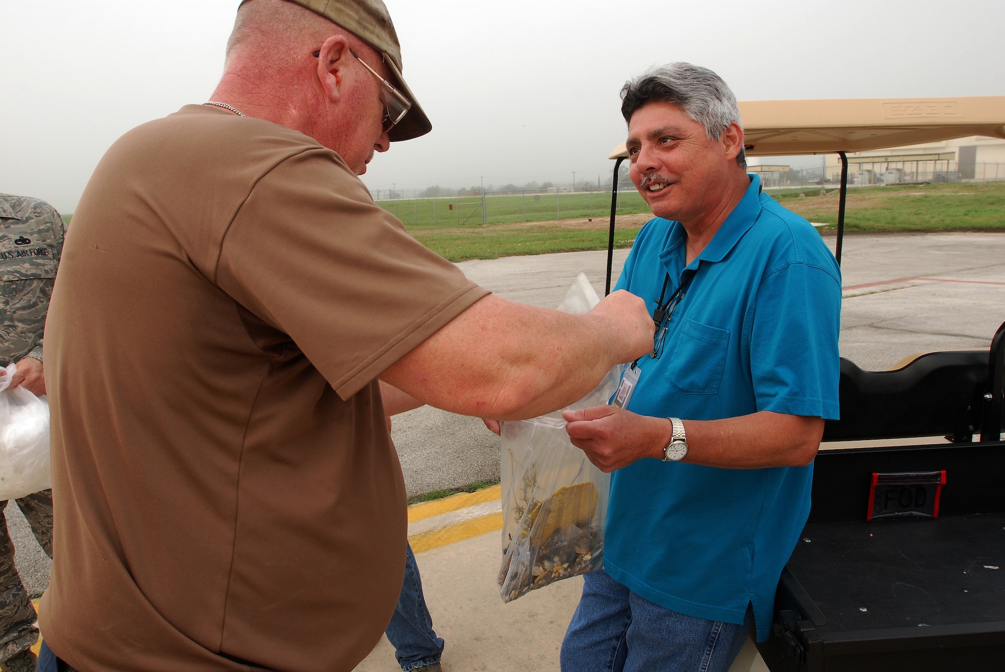 Members of the 433rd Airlift Wing, Lackland Air Force Base, Texas, walk the flightline in a Monday morning ritual searching for foreign object debris. 

Nick Peche, 433rd Maintenance Group holds a plastic bag open while James Goluke, 433rd Maintenance Squadron dumps a handful of debris he picked up.
Everyone from Col. Kenneth Lewis, wing commander,  to the brand new airman basics participate. The FOD is collected in a bag and properly disposed of. The wing vice commander Col. Dale Andrews, hides a gold-painted bolt somewhere to be found as incentive to be thorough during the FOD walk. Whomever finds the golden bolt wins their 15 minutes of fame and thanks from the roaring jet engines. (U.S. Air Force photo Airman 1st Class Brian McGloin)
