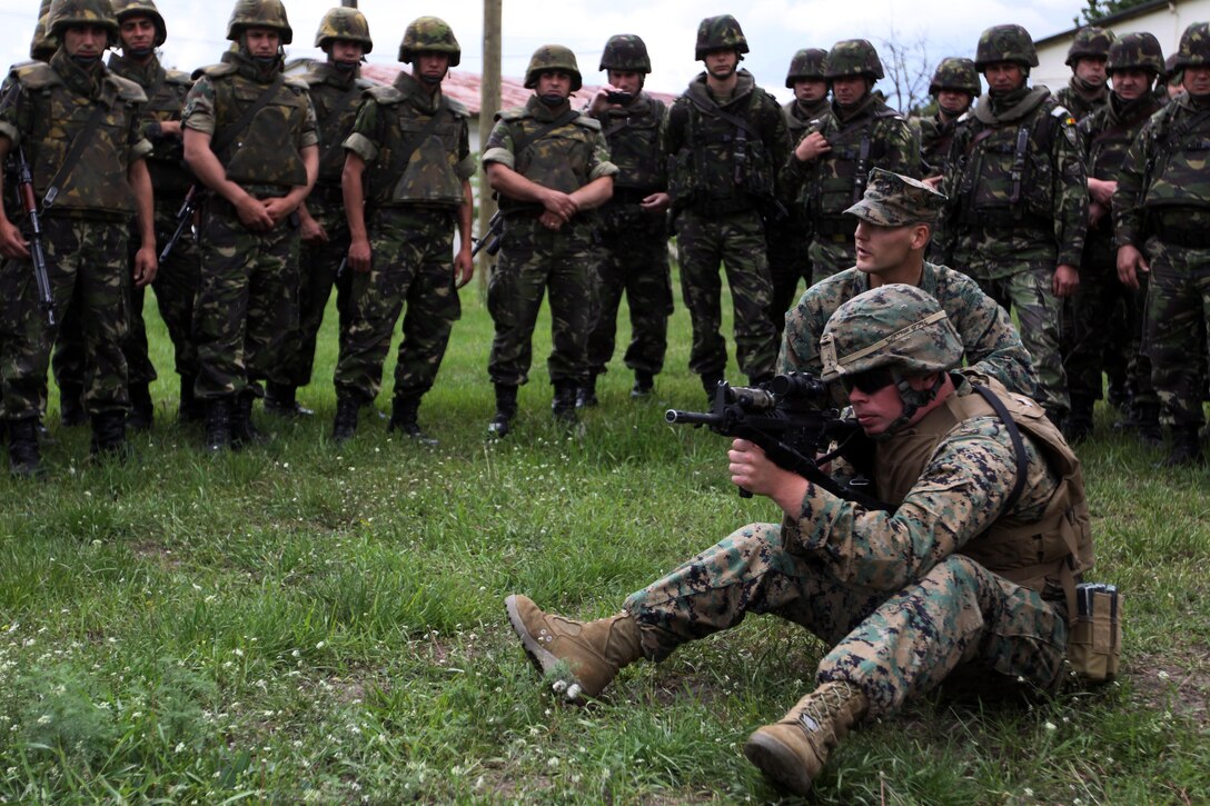 Romanian Marines look on as Lance Cpl. Jesse Watson, an assaultman with scout platoon, Headquarters and Service Company, 1st Tank Battalion, demonstrates the sitting firing position at Babadag Training Area, Romania, May 18. The Marines of scout platoon taught the Romanians how to properly position themselves while firing as well as other combat marksmanship techniques.