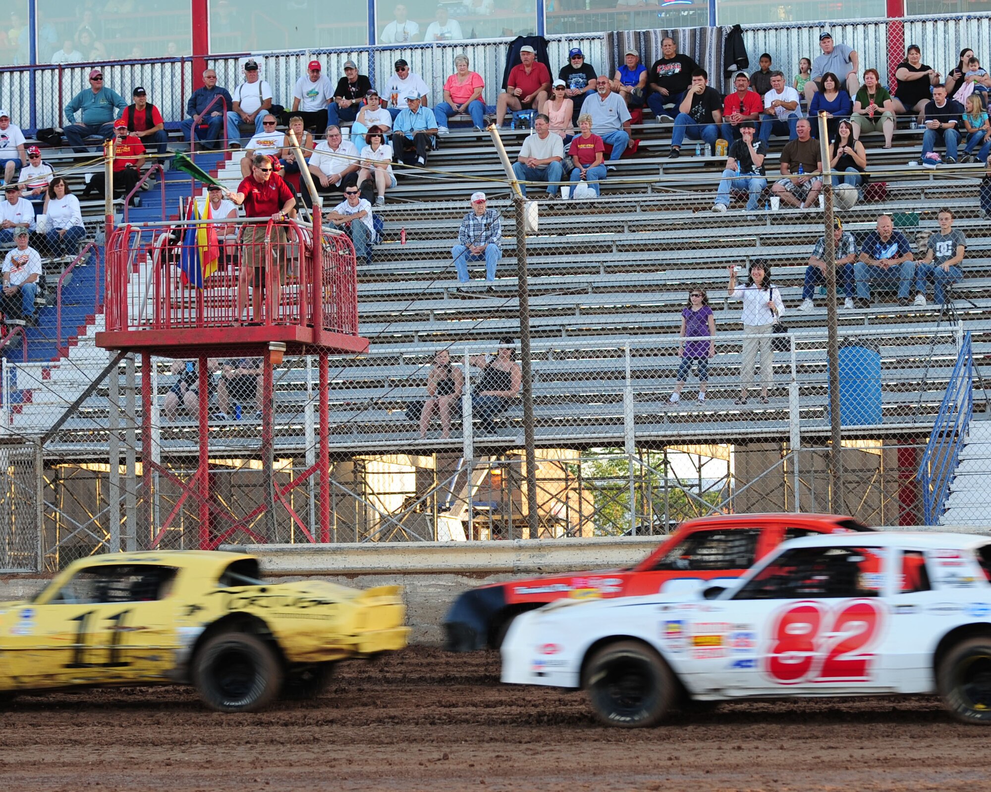 Racecars speed pass the starting line as Col. Charles Hunter, 355th Mission Support Group commander, waves the starting flag at the USA Raceway track May 15. This year marked the second annual USA Raceway Military Appreciation night, honoring the men and women of the armed forces. (U.S. Air Force photo/Airman Jerilyn Quintanilla)