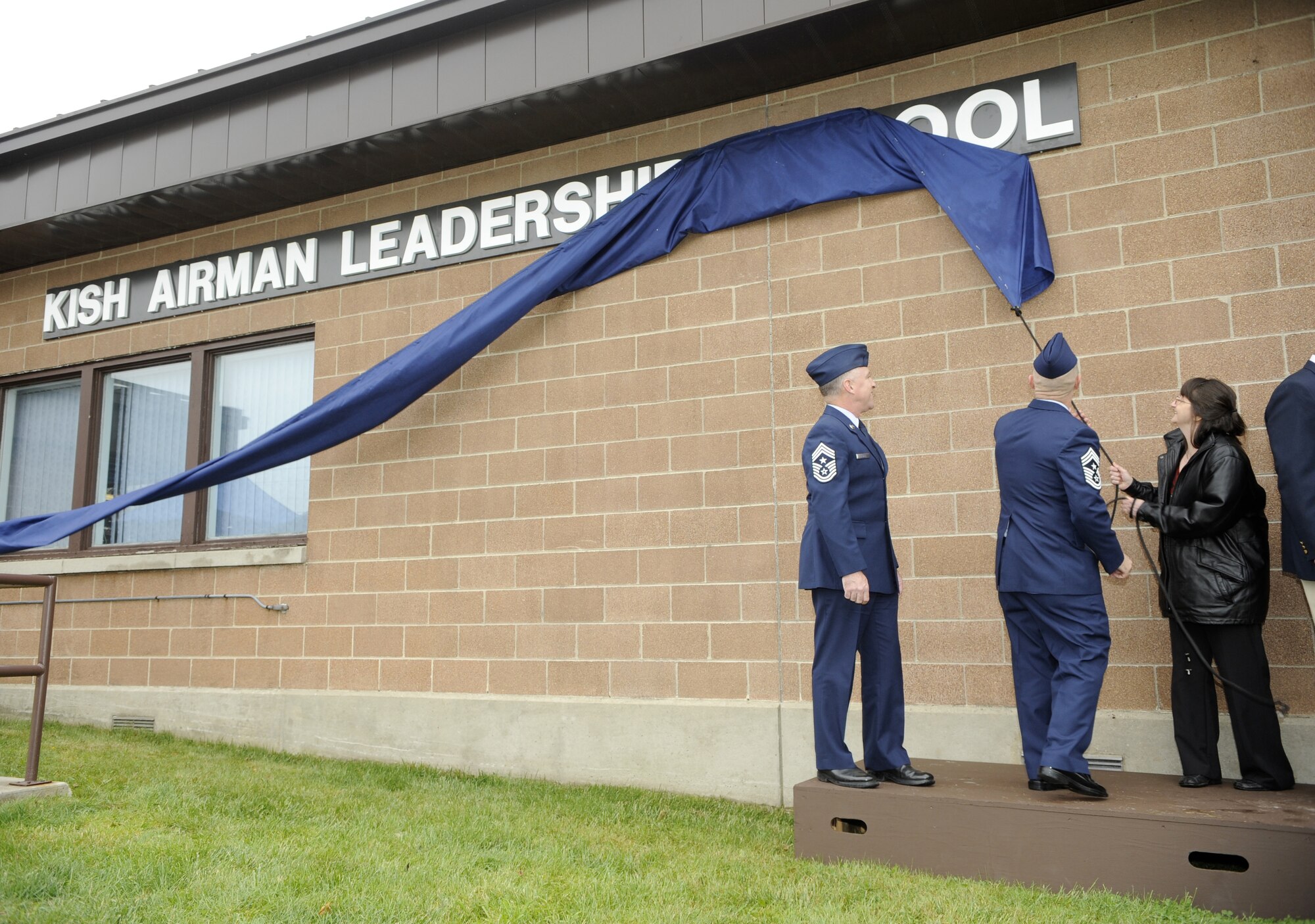 Betsy Kish, daughter of Tech. Sgt. Frank Z. Kish, pulls the draw string with the help of Chief Master Sgt. Lee Wofford, 87th Air Base Wing command chief, to reveal the Airmen Leadership School’s new name at a ceremony May 12. The ALS building was renamed “Kish Airman Leadership School” in memory of Tech. Sgt. Frank Z. Kish who served as Maj. Thomas B. McGuire’s maintenance crew chief during World War II. (U.S. Air Force photo/Carlos Cintron)