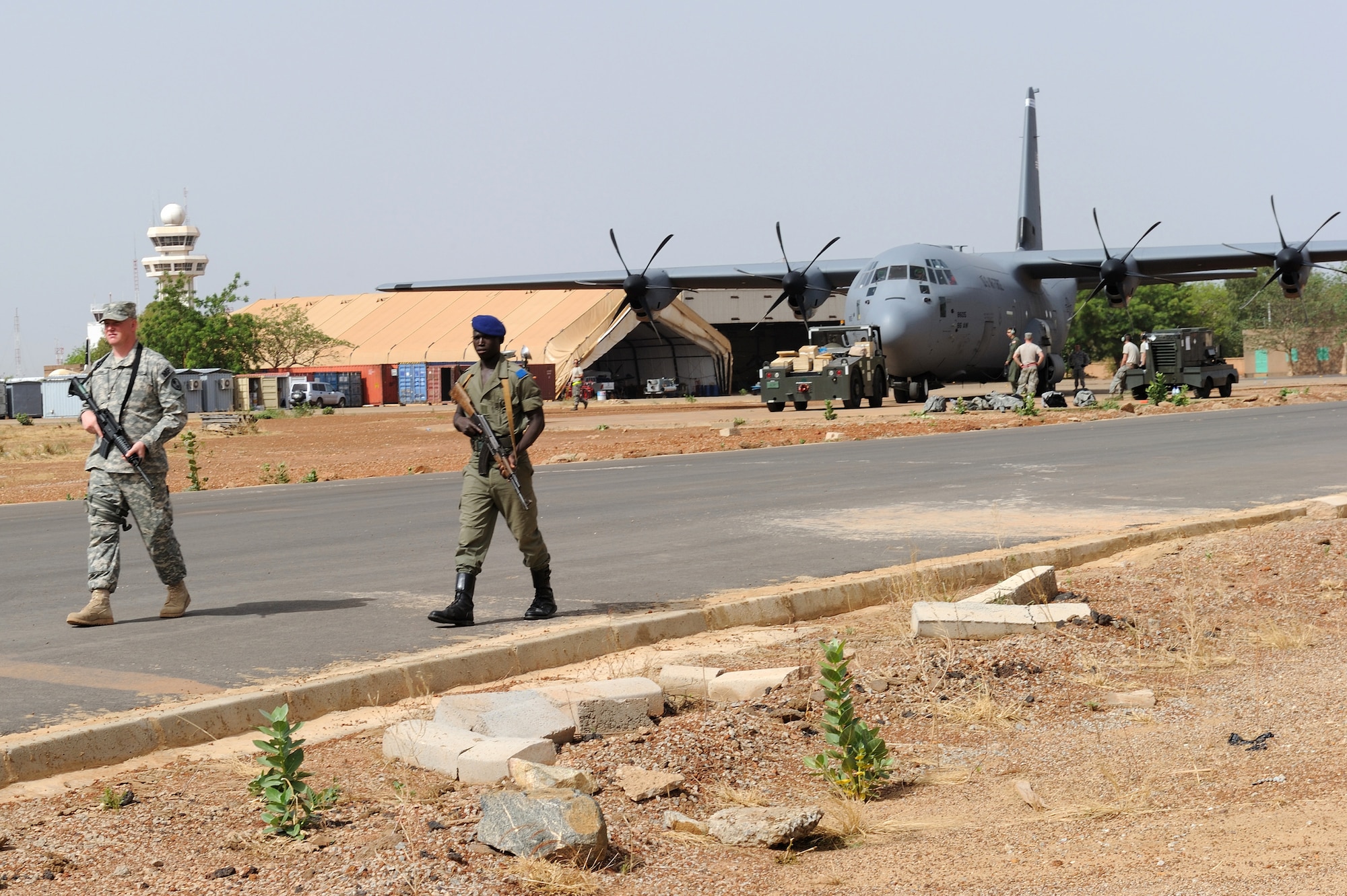 A joint U.S. Army and Burkinabe army security patrol provides airfield security while a C-130J Super Hercules prepares for departure with Burkinabe soldiers and equipment onboard for deployment to Mali in support of Exercise Flintlock 10 May 1, 2010, in Ouagadougou, Burkina Faso. The C-130J is deployed from Ramstein Air Base, Germany. (U.S. Air Force photo/Master Sgt. Jeremiah Erickson)