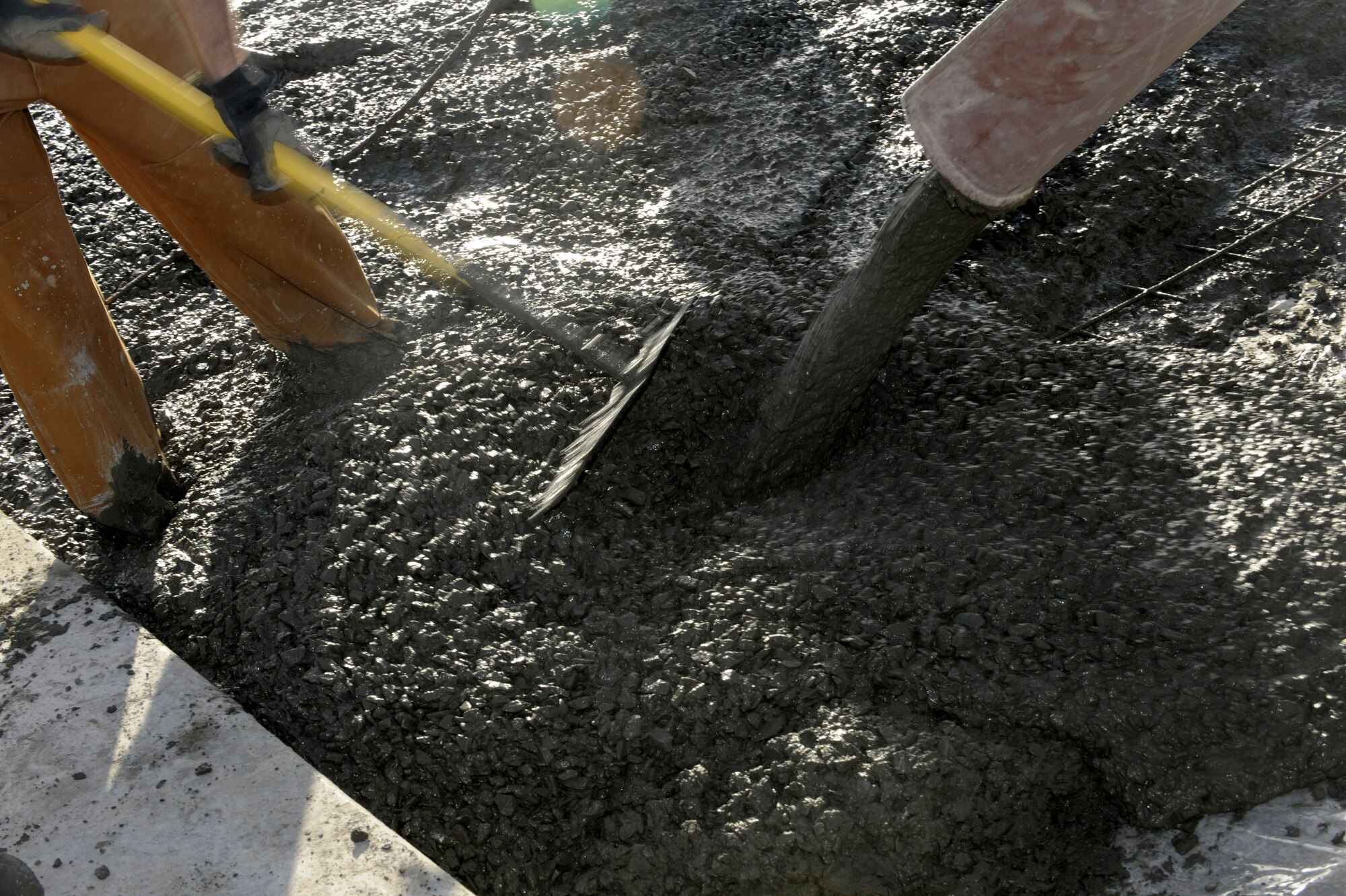 As concrete pours, members of the 809th Expeditionary Red Horse Squadron work rapidly to smooth out the concrete evenly and efficiently the large area maintenance shelter (LAMS) pads for aviation maintenance.  (U.S. Air Force photo by Senior Airman Nancy Hooks/Released)