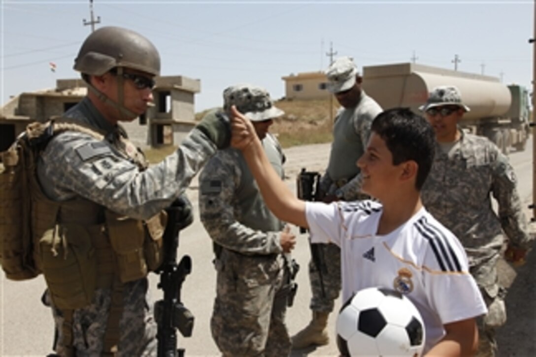 U.S. Navy Master Chief Petty Officer Jerry Woller of Joint Combat Camera- Iraq and a local Iraqi boy share a fist pound after the boy received a soccer ball from soldiers assigned to 2nd Battalion, 3rd Field Artillery Regiment, 1st Heavy Brigade Combat Team, 1st Armored Division, in Shwan, Iraq, on May 8, 2010.  The 2nd Battalion, 3rd Field Artillery Regiment and Bravo Company, 414th Civil Affairs Battalion visited villages around Kirkuk to gather atmospherics by meeting and speaking with the locals about current conditions in the area.  