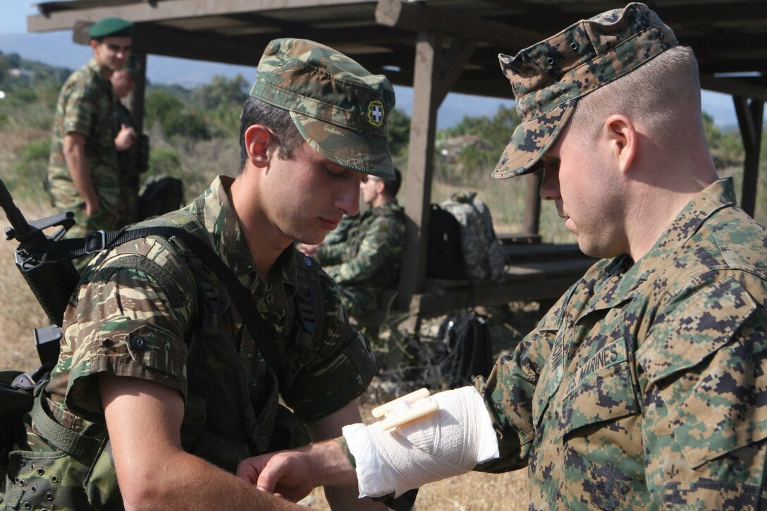 Lance Cpl. Kevin Cronin, a rifleman with the Security Cooperation Marine Air Ground Task Force, Africa Partnership Station 10, helps a member of 1st Paratrooper Battalion, Greek Special Forces, during a combat lifesaving practical application at Maleme, Crete, May 20.  The Greek Special Forces and SCMAGTF spent the day conducting bilateral training exercises, to include a live-fire range, weapons handling classes, and combat lifesaving.