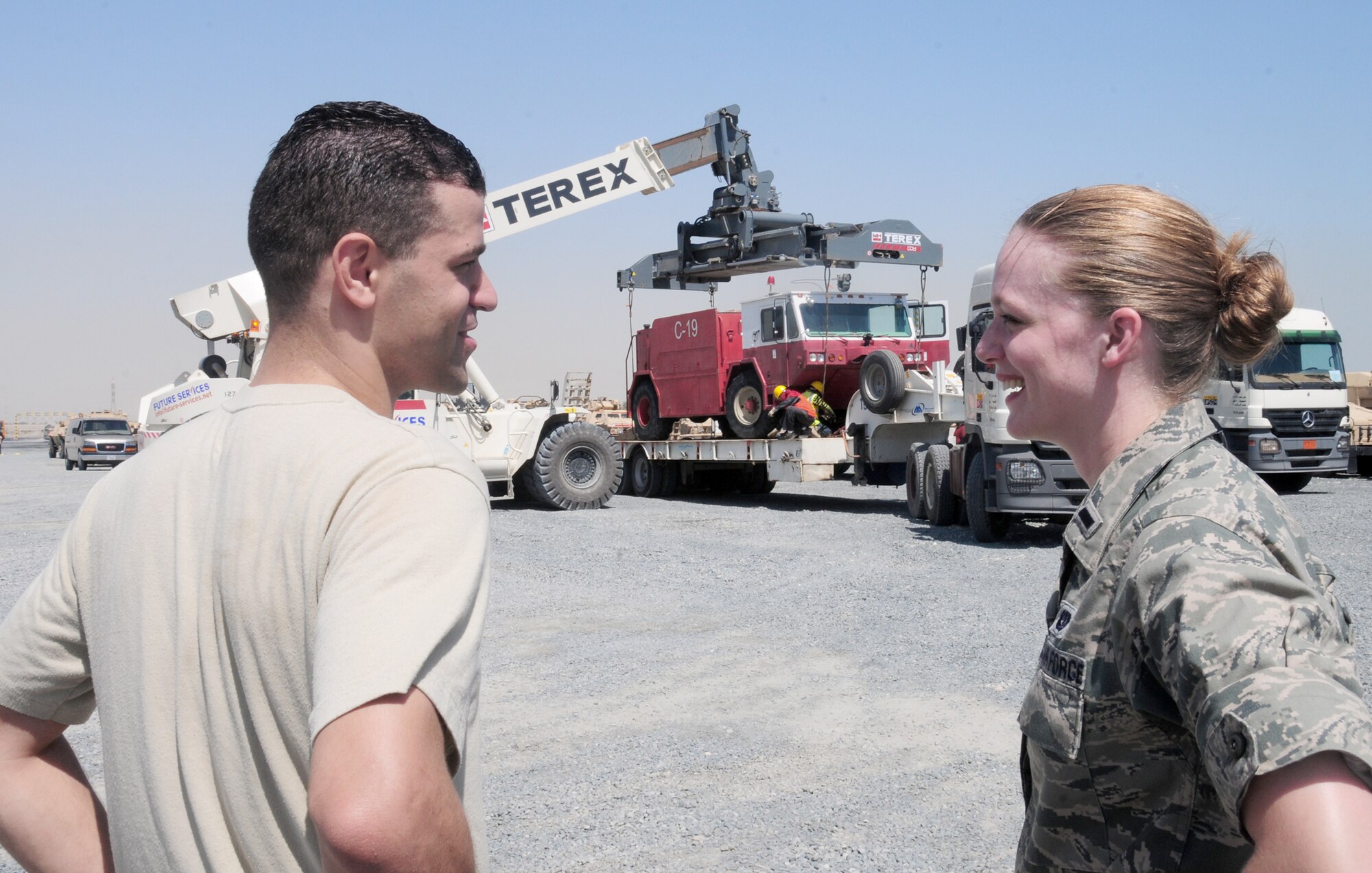Staff Sgt. Joseph Jacovina and 1st Lt. Elise Jones discuss the movement of an Air Force fire truck May 4, 2010, at an undisclosed location in Southwest Asia, while contractors load the asset onto a truck to be taken to the nearby seaport. Sergeant Jacovina and Lieutenant Jones are U.S. Air Forces Central Command liaison officers. They coordinate sea-based shipments of oversized military equipment in and out of the USAFCENT area of responsibility. (U.S. Air Force photo/Staff Sgt. Lakisha A. Croley)