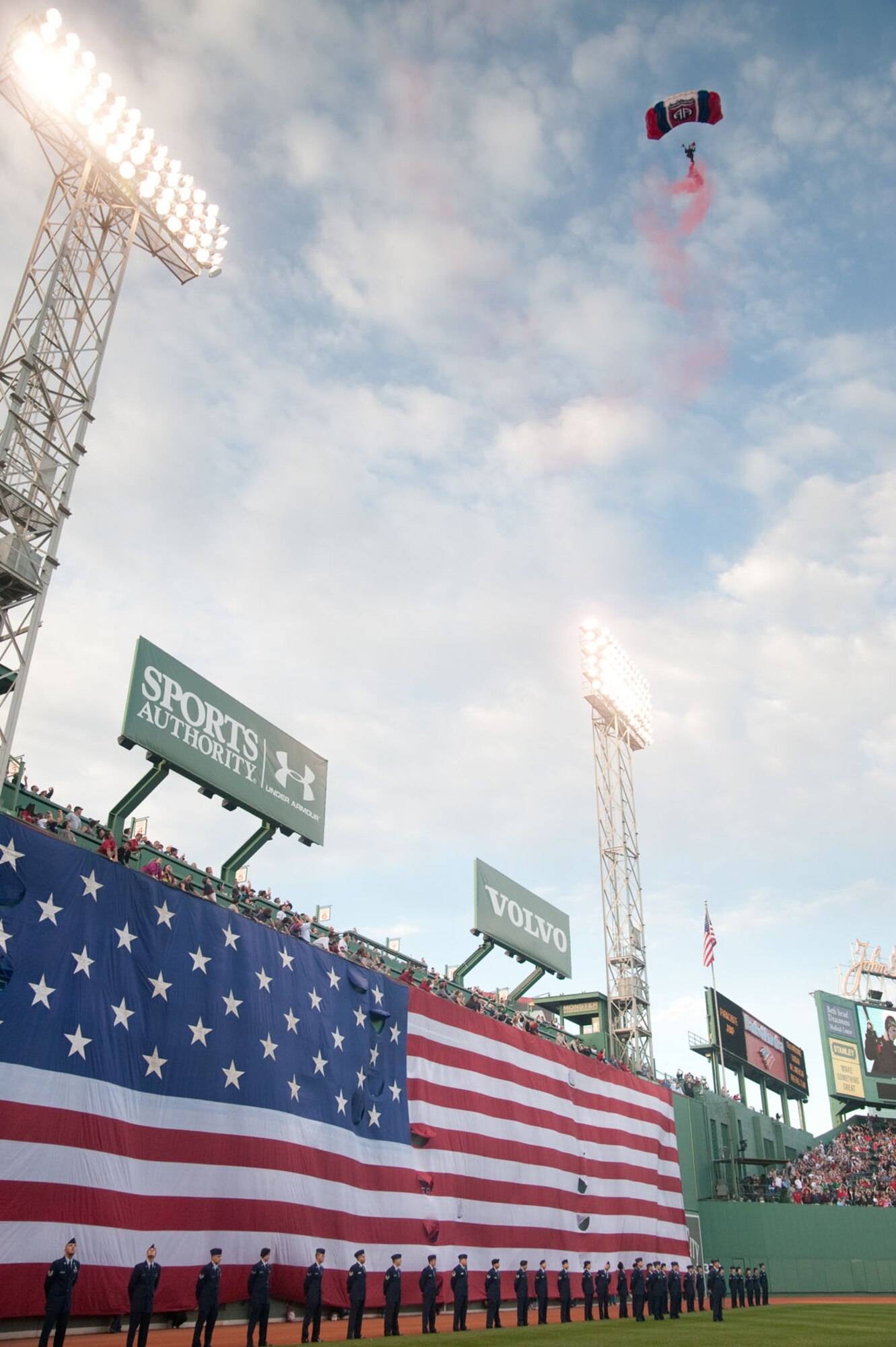 BOSTON – Hanscom Air Force Base Airmen stand in front of the flag as a paratrooper from the 82nd Airborne Division, All American Freefall Team, prepares to land in Fenway Park. (U.S. Air Force photo by Mark Herlihy)