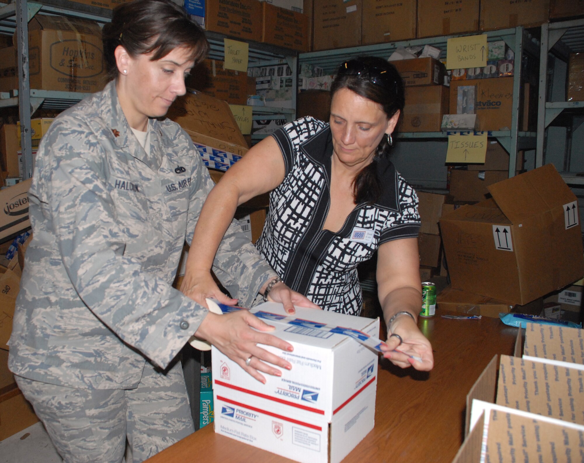(Left to right) Maj. Stephanie Halcrow, 436th Aircraft Maintenance Squadron commander, and Joan Cote, executive director of United Service Organizations Delaware, help to make boxes for care packages with Dover military spouses to send to Dover Airmen downrange. (U.S. Air Force photo/Airman 1st Class Shen-Chia Chu)