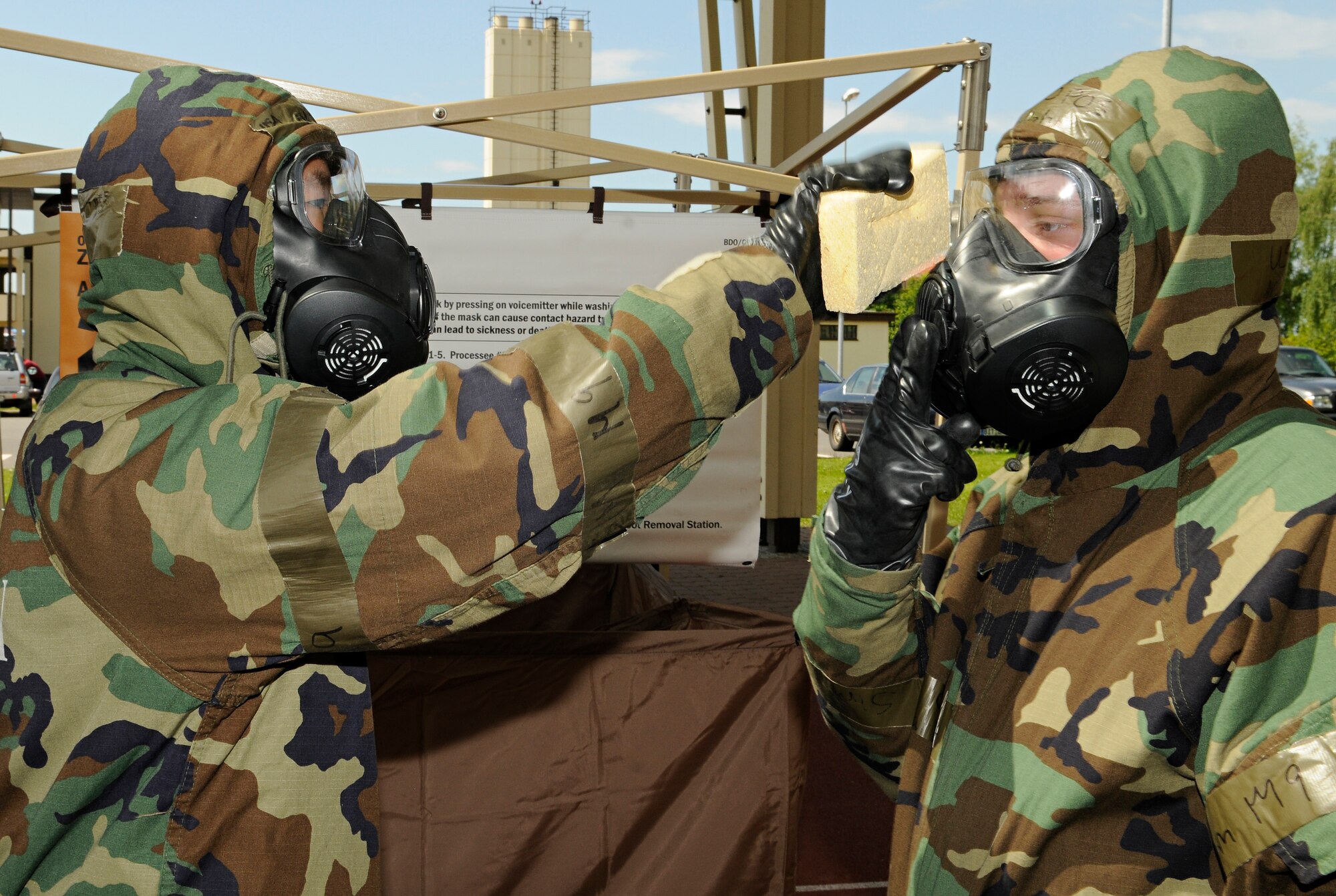 SPANGDAHLEM AIR BASE, Germany – Airman 1st Class Raymond Kim, 52nd Component Maintenance Squadron, uses a simulated bleach solution to wash Airman 1st Class Chris Gallaher’s, 52nd Equipment Maintenance Squadron, mask as they process through a contamination control area May 20. The CCA was set up for a one-day exercise in preparation for the NATO Force Evaluation. (U.S. Air Force photo/Senior Airman Benjamin Wilson)