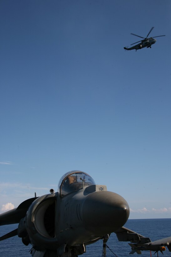 An AV-8B Harrier of Marine Attack Squadron 223 sits on the flight deck of the Ark Royal, the British Royal Navy’s flagship aircraft carrier, while a Royal Navy Sea King flies in the distance, May 22.::r::::n::“Exercise Capella Strike was an exciting opportunity to integrate American air power with British sea power,” said Capt. Nicholas R. Wineman, a pilot with VMA-223.::r::::n::