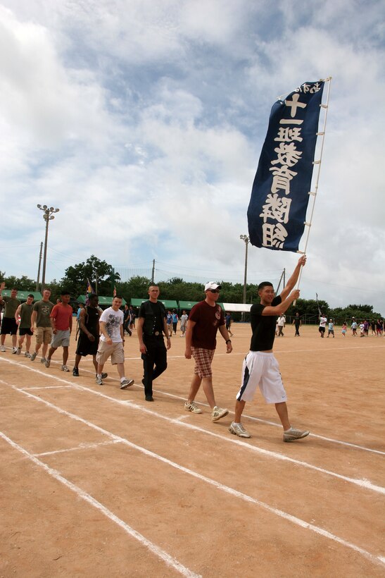 Marines parade around the sports field at the 37th annual Sports Day in Henoko May 23, with the eleventh section flag of Henoko Village, Camp Schwab. The Marines have::r::::n::participated in the Sports Day since its inception in 1973.