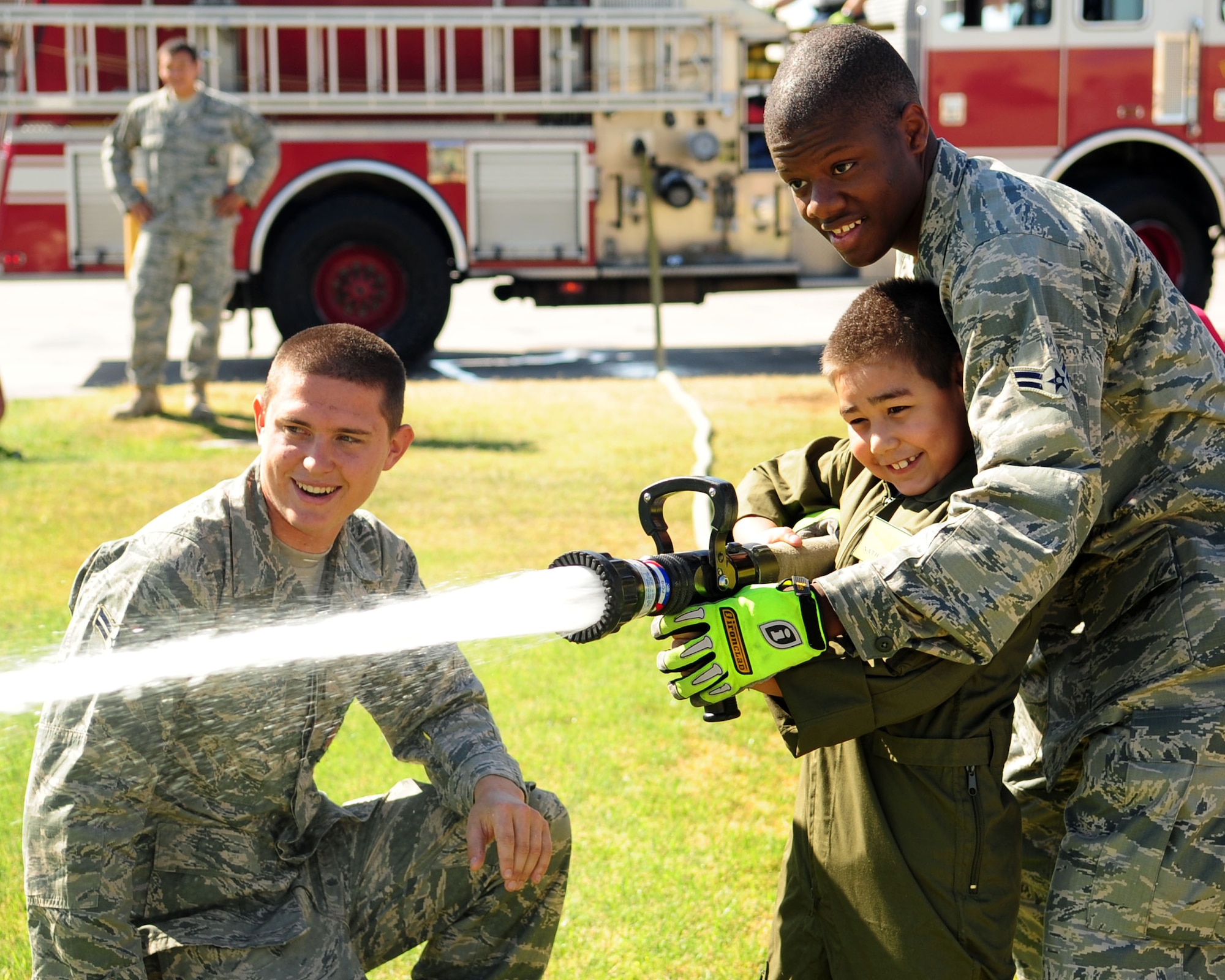 Airman 1st Class Michael Neal and Airman 1st Class Sean Piper, both firefighters from the 355th Civil Engineer Squadron, help Nathan Hoffmann hold a water hose steady during his Pilot for a Day tour here May 21. As part of his tour, Nathan and his family got to see parts of the base to include the 357th Fighter Squadron, the air traffic control tower, the D-M Fire Department and several aircraft static displays. (U.S. Air Force photo/Airman Jerilyn Quintanilla)