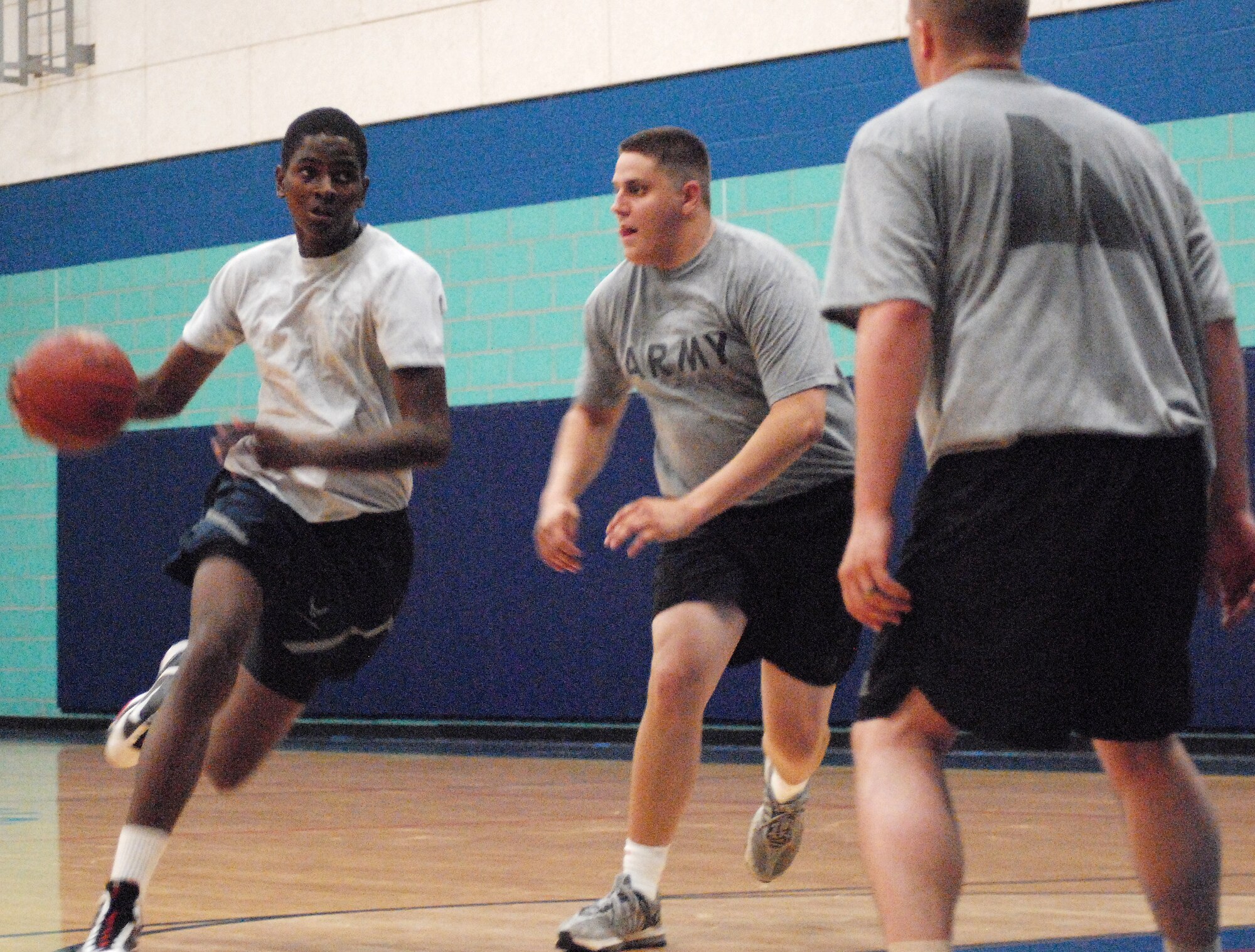 Airman Enoma Ighedosa drives past two 344th Military Intelligence Battalion players during the sports days 3 on 3 basketball tournament.  Sports day provided a variety of activities for all participants including volleyball, tennis, swimming and more. (U.S. Air Force photo/Master Sgt. Randy Mallard)