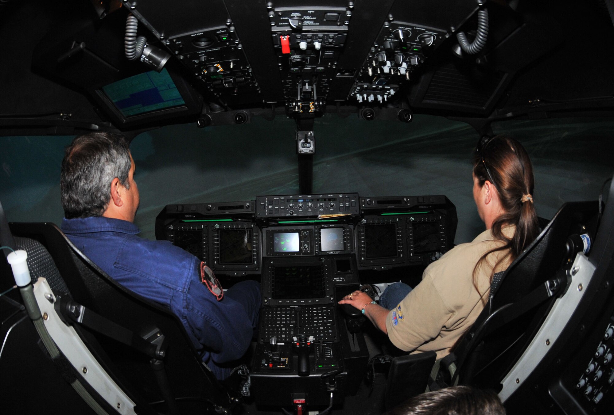 Brian Smith, a contractor with Lockheed-Martin, guides a news reporter during a simulated CV-22 Osprey flight over a virtual Clovis, N.M., May 26. The $25 million simulator can be programmed to display any location and  weather conditions.r saves the Air Force money during its operational liftetime. (U.S. Air Force photo by Airman 1st Class Maynelinne De La Cruz)