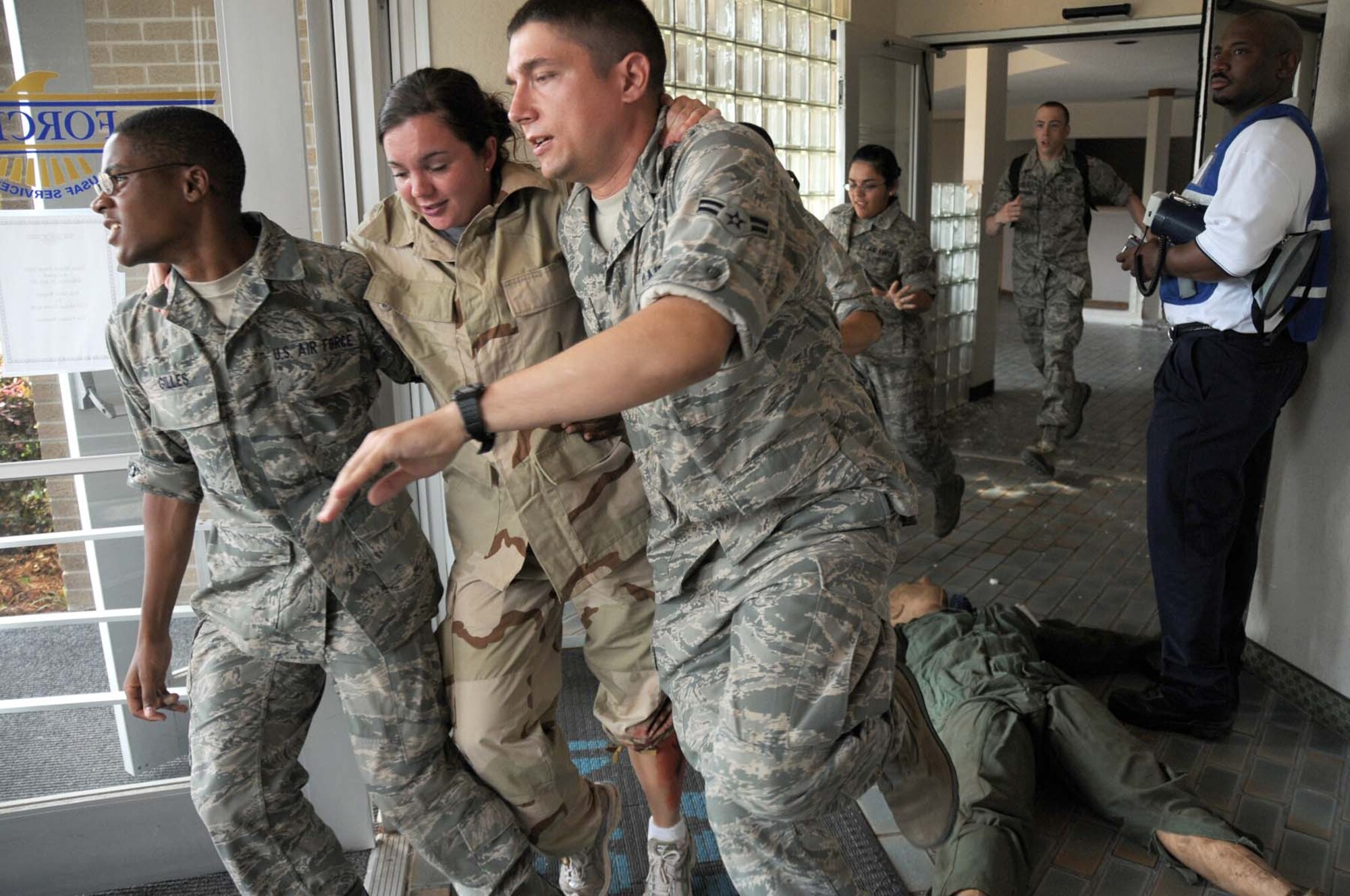 From left, Airman Basic Jahaui Gilles, Airman Katie Ewel and Airman 1st Class Alexander Tarnawski exit Muse Manor under the watchful eye of exercise evaluation team member Darrin McClure during an active shooter exercise May 20.  Airmen Gilles and Ewel are students in the 334th Training Squadron, and Airman Tarnawski is a student in the 336th TRS.  (U.S. Air Force photo by Kemberly Groue)