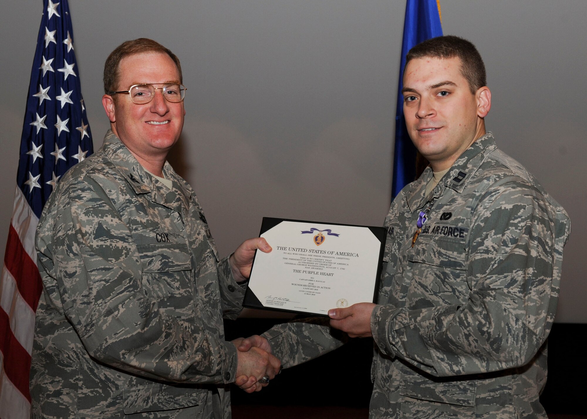 MINOT AIR FORCE BASE, N.D. -- Capt. Erik Rauglas, 5th Civil Engineer Squadron readiness and emergency management officer, receives a Purple Heart from Col. Douglas Cox, 5th Bomb Wing commander, at the base theater here May 26. Capt. Rauglas was injured while deployed to Afghanistan as commander of Provinical Reconstruction Team Nangarhar’s Quality Assurance/Quality Control mission. On Jan. 6, 2010, Captain Rauglas was on a dismounted patrol performing a construction inspection an ongoing road project. While on the patrol a tank mine exploded. Captain Rauglas received several shrapnel injuries on left shoulder and both legs.(U.S. Air Force photo by Tech. Sgt. Lee A. Osberry Jr.)