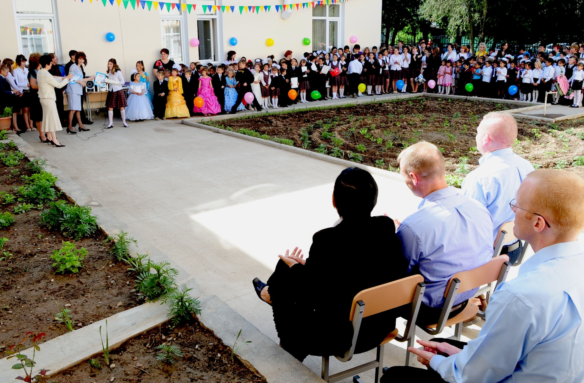 Airmen from the Transit Center at Manas, Kyrgyzstan, watch as children from Birdik Village School receive certificates culminating the successful completion of the school year May 25, 2010. The school celebrated its ribbon cutting just eight months ago after a reconstruction project valued at more than $540, 000. The newly-renovated school consists of 15 new computers, several TV systems, chairs, lockers, green boards, a new kitchen, a cafeteria, a transformer, and an electric generator, along with newly-installed furniture and equipment to help the children learn in a more conducive environment. (U.S. Air Force photo/ Senior Airman Nichelle Anderson/ released)