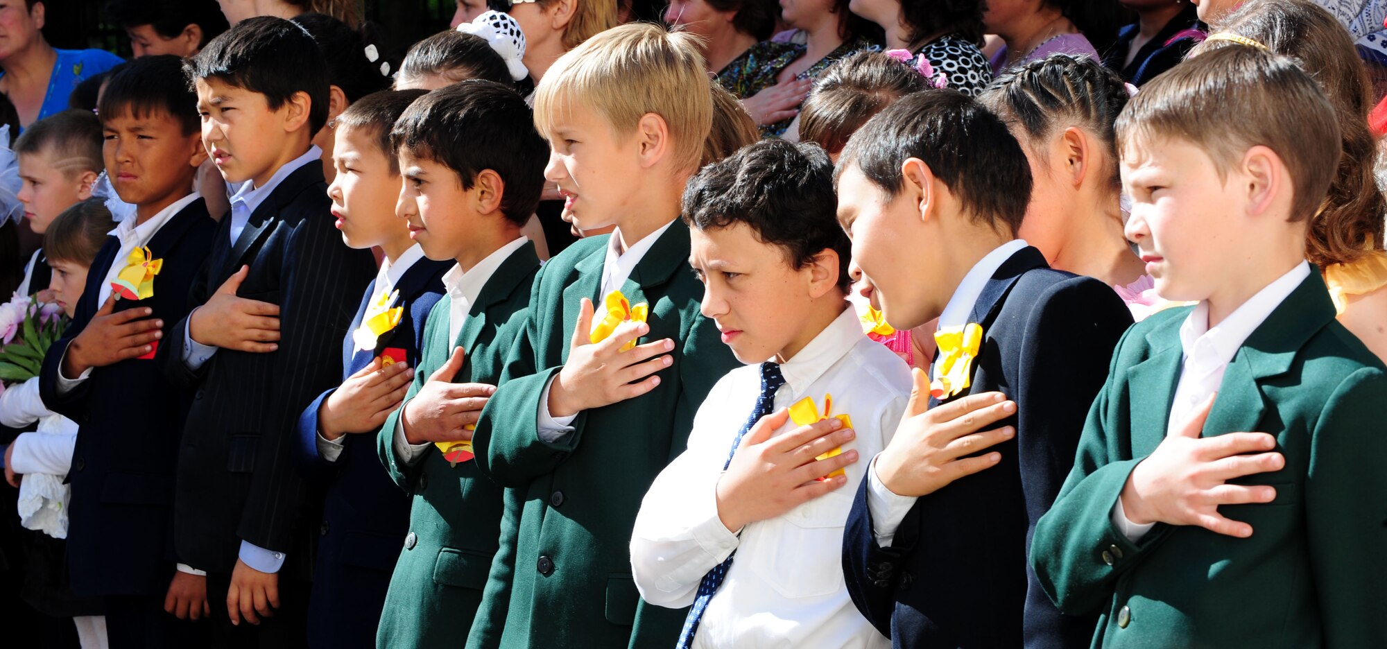 Children place their hands over their hearts during the playing of the Kyrgyz National Anthem marking the beginning the graduation ceremony of the Birdik Village School, Kyrgyzstan, May 25, 2010. Airmen from the Transit Center at Manas, Kyrgyzstan, attended the ceremony to celebrate the accomplishments of the children during the school year. This year was important to the children and the community of Birdik Village because they celebrated the completion of the first school year in the renovated facility. The project, which cost about $540,000, was funded by the Air Force and made possible by volunteer efforts from Airmen at the Transit Center at Manas, Kyrgyzstan. The ribbon cutting was held Sept. 1, 2009.