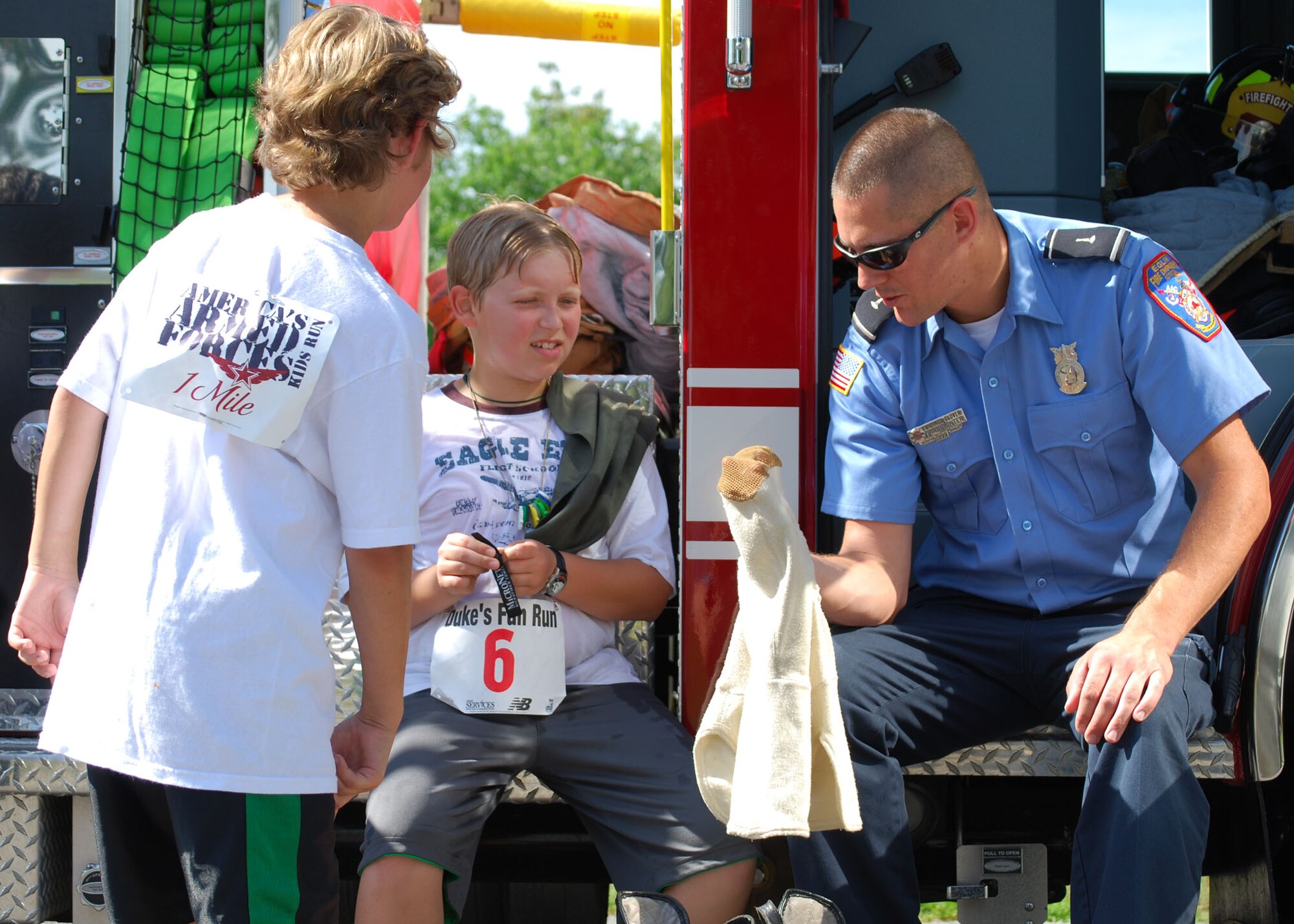 Duke Field firefighter Michael Glover explains part of his protective ensemble for (from left) Evan Bragg and Michael Dunn following the annual Duke Field Kids’ Fun Run and Adult 5K May 15.   The firefighters provided standby emergency medical support for the runners.  The event coincided with the Air Force-wide America’s Armed Forces Kids’ Run.    First-place finishers by respective age category included:  Nicholas Ruiz, 5-6 half mile; Faith Alexander, 7-8 half mile;  Austin Bonebrake, 9-13 one mile; Eric Bonebrake, adult 5K.  (U.S. Air Force photo/Tech. Sgt.  Cheryl Foster)