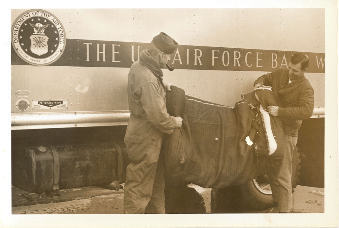 John Hickox and William “Red” Brower roll up a sleeping bag outside of The USAF Band truck.  They often augmented the crew, assisting with the set-up and tear-down of equipment. If you have further stories you can share about this photo, please email our Band Historian <a href="mailto:usafbandhistorian@afncr.af.mil">Technical Sgt. Tracey MacDonald</a>. Thank you and we look forward to hearing from you!  This is Photo 31. (Unknown Photographer)