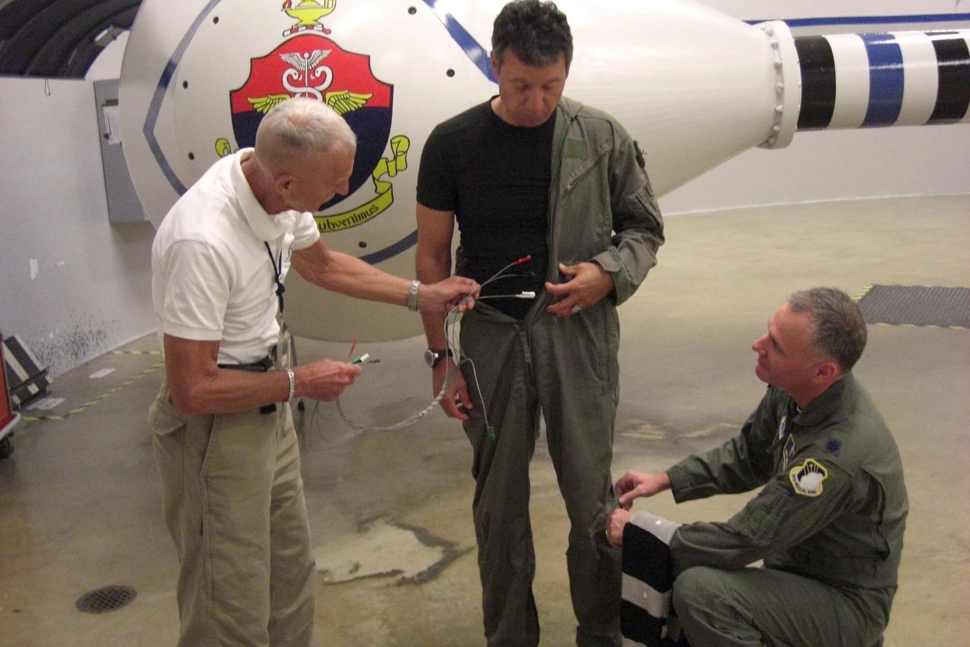 Lt. Col. Lance Annicelli (right) and Dr. Ulf Balldin (left) fit retired Capt. James Kisner with a prototype muscle stimulation suit on May 25 to perform a centrifuge test as part of an acceleration protection research project they are conducting at Brooks City-Base, Texas. The three men designed a garment which will be worn by pilots that will automatically sense and contract lower body muscles during and throughout excessive G-forces during flight.  (U.S. Air Force photo by Durrell Bess)