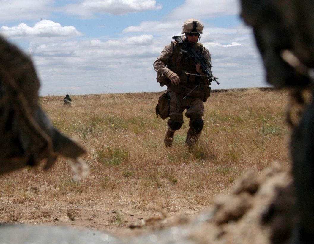 A machine gunner from Company K, 3rd Battalion, 25th Marine Regiment rushes behind the cover of sandbags during a firing and maneuvering dry run.