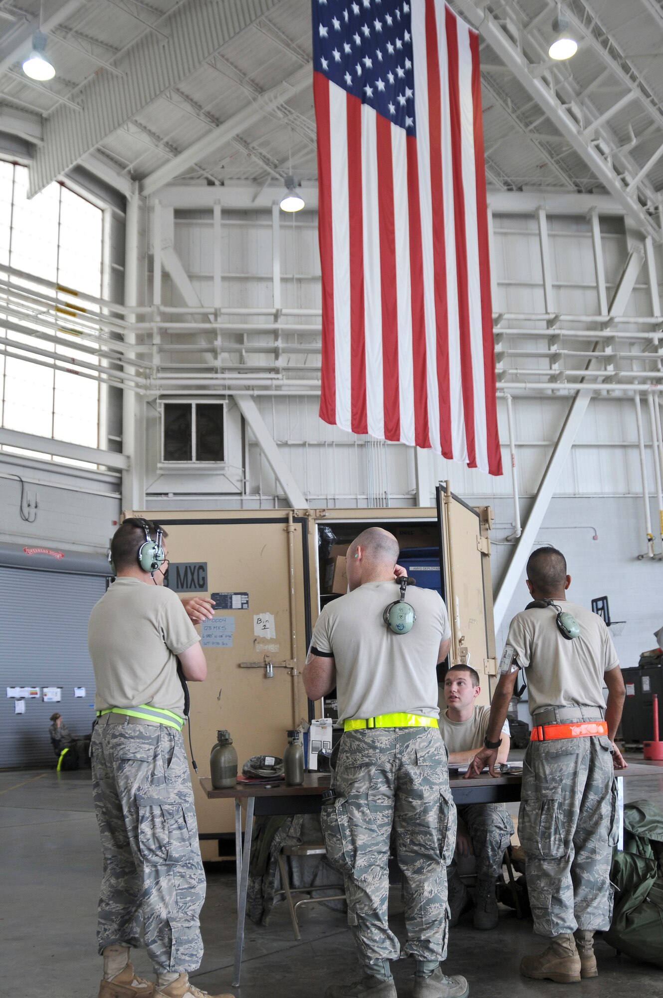 Air cargo specialists from the notional 104th Air Expeditionary Wing discuss their upcoming duties May 19, 2010 while standing in front of a large American Flag inside the Main Hanger at the Gulfport Combat Readiness Training Center in Gulfport, Miss. Airmen from the Kentucky Air National Guard's 123rd Airlift Wing, the active-duty Air Force's 317th Airlift Group at Dyess Air Force Base, Texas, and the Air Force Reserve's 70th Aerial Port Squadron from Homestead Air Reserve Base, Fla., all combined to form the 104th during an Air Mobility Command Operational Readiness Inspection here. (U.S. Air Force photo/Tech. Sgt. Dennis Flora) (Released)