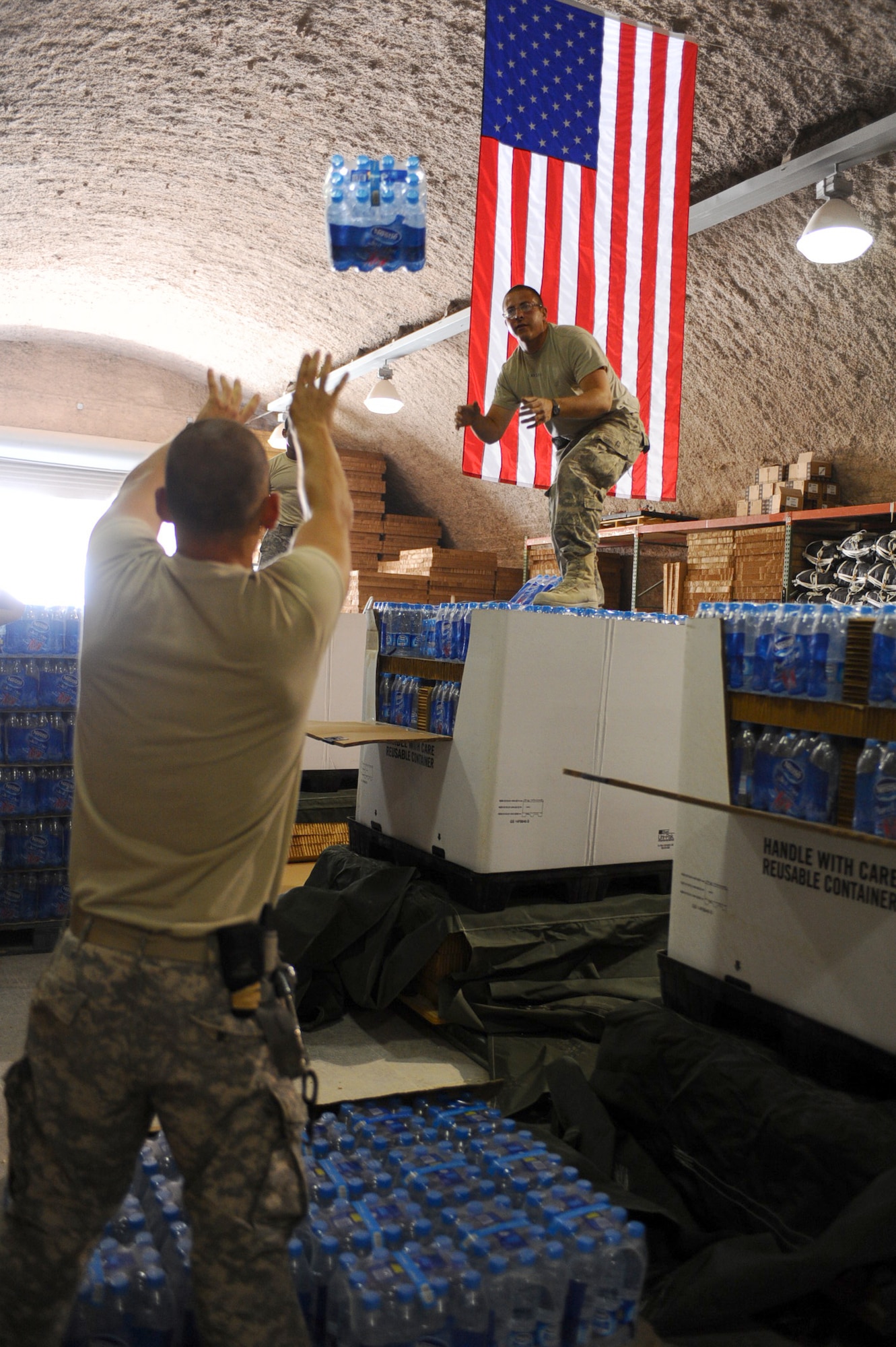 Army Sgt. Anthony Hopkins (left) tosses a pack of water to Spc. Patrick Vinzani to be loaded onto a pallet at a non-disclosed Southwest Asia location May 19, 2010. Both Soldiers are 824th Quartermaster Company, Det. 9, parachute riggers. The 824 QM CO prepares supply pallets and parachutes for air drop deliveries to Iraq and Afghanistan. (U.S. Air Force photo by Senior Airman Kasey Zickmund)[RELEASED]