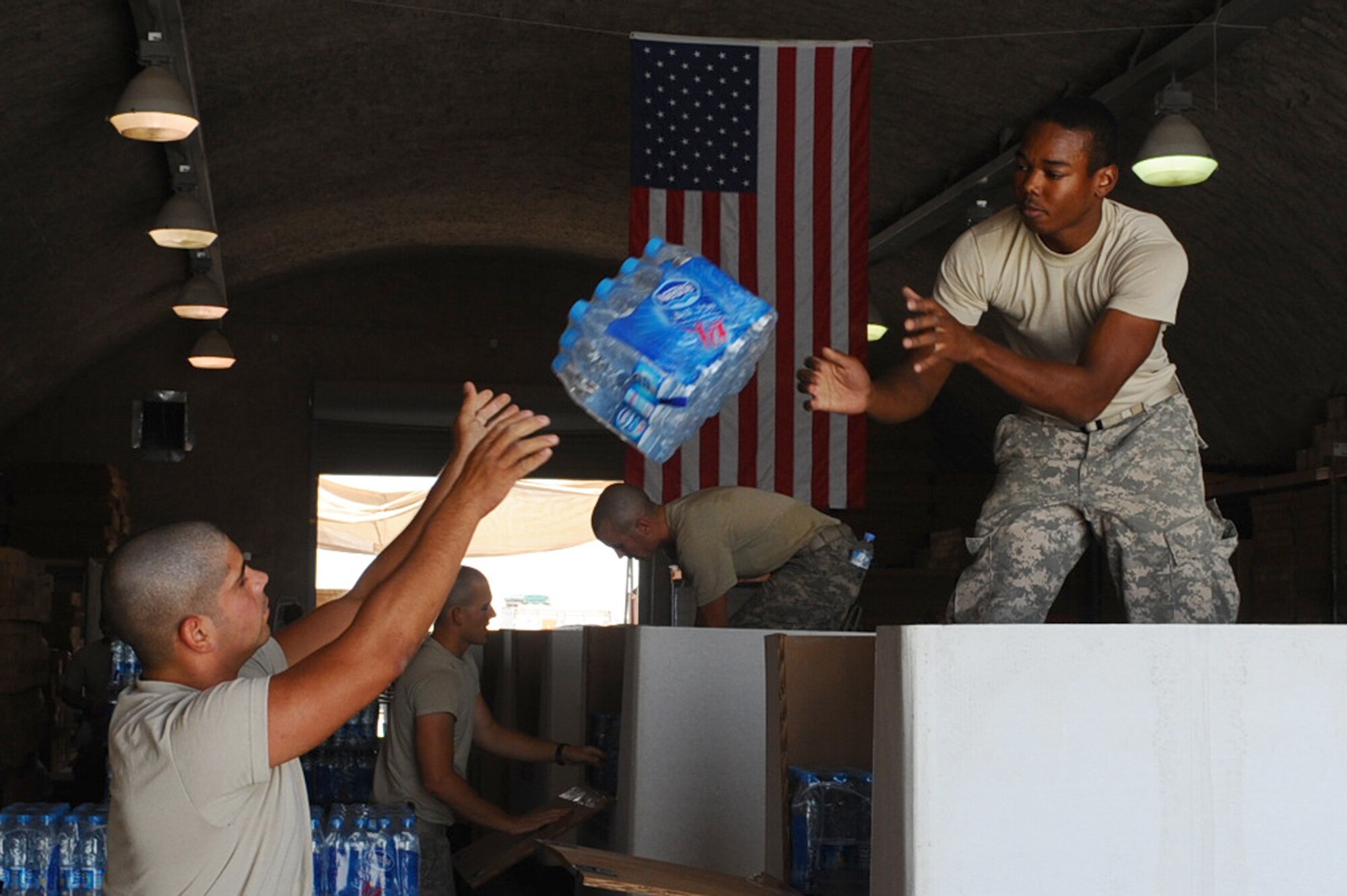 Spc. Claudio Ortiz (left), 824th Quartermaster Company, Det. 9 rigger, tosses a pack of water at a non-disclosed Southwest Asia location May 19, 2010, to Pfc. Johnpaul Wallace (right), 824 QM CO, Det. 9 rigger, rigger, while packing a bundle for air drop to forward-deployed servicemembers. (U.S. Air Force photo by Senior Airman Kasey Zickmund)[RELEASED]