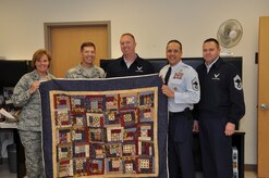 Tech. Sgt. Dan Hunt (center), 436th Medical Support Squadron accepts a Quilt of Valor from Col. Thomas C. Joyce, Air Force Mortuary Affairs Operations commander, for his support of the mortuary mission. For four years Sergeant Hunt X-rayed the remains of more than 3,000 fallen servicemembers, trained incoming personnel who deployed in support of the mission and was actively involved in preparing for and providing training for a new CT scanner and X-ray room. Colonel Joyce thanked him for his support and reiterated the importance of the partnership between the mortuary and the 436th and 512th Airlift Wings. (U.S. Air Force photo/Christin Michaud)