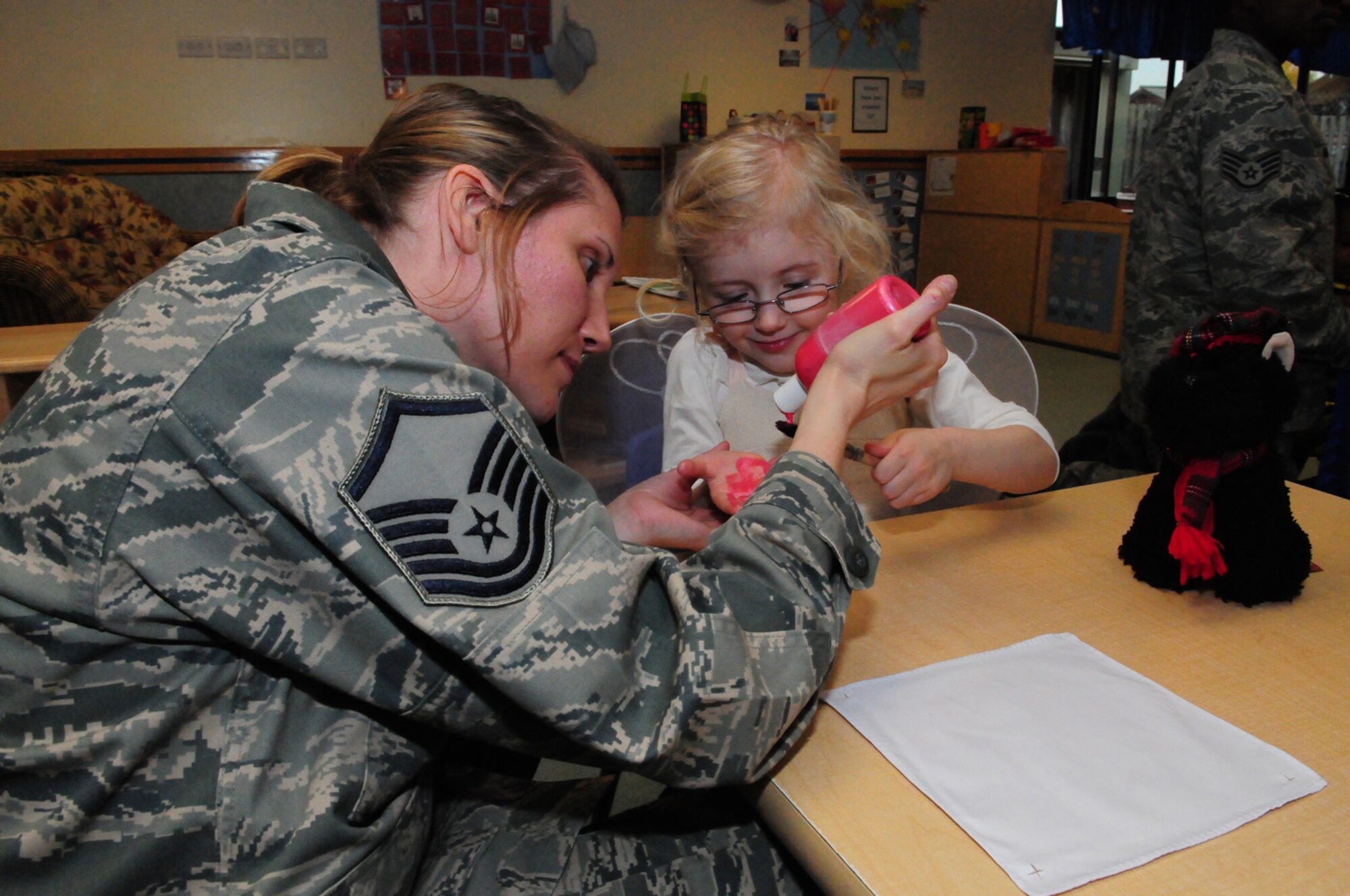 RAF MILDENHALL, England -- Rachel DeMarco, 3, holds out her paintbrush as her mom, Master Sgt. Tracy DeMarco, 100th Air Refueling Wing Public Affairs, squirts paint onto it to make hand prints. This was just one of many activities children in the child development center participated in at the Fall Festival Oct. 29, 2010. It was the first joint partnership event between the CDC and the parent advisory committee. All children were given a free pumpkin and treat bag, filled with goodies from both the PAC and the CDC. (U.S. Air Force photo/Karen Abeyasekere)