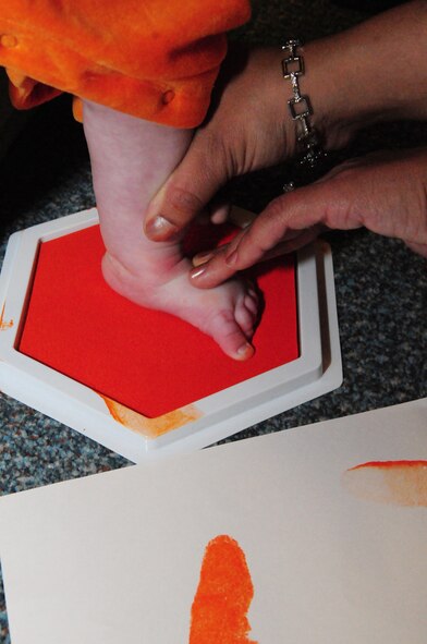 RAF MILDENHALL, England -- Kayla Lovegreen, 4 months, has her foot painted by mom, Tech. Sgt, Rosa Lovegreen, 7th Special Operations Squadron, as she makes footprints on a sheet of paper as part of the Fall Festival Oct. 29, 2010, at the child development center. This was the first joint partnership event between the CDC and the parent advisory committee. The PAC provided pumpkins for each class to decorate, along with smaller pumpkins for two pumpkin patches. (U.S. Air Force photo/Karen Abeyasekere)