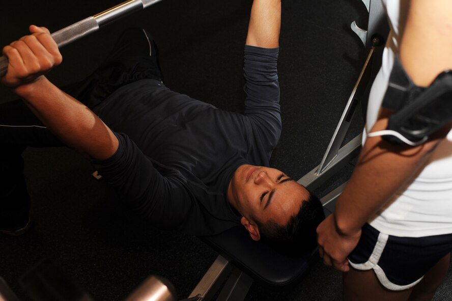 MINOT AIR FORCE BASE, N.D. -- Airman Ian Carrion, 5th Operations Support Squadron air crew flight equipment, warms up as Airman 1st Class Monica Diaz De Lope-Diaz, 5th OSS air crew flight equipment, spots him before starting his weight lifting routine at the McAdoo Sports and Fitness Center here Nov. 3. It is important to ensure an ample amount of strength training is incorporated into time spent at the gym. (U.S. Air Force photo by Airman 1st Class Aaron-Forrest Wainwright)