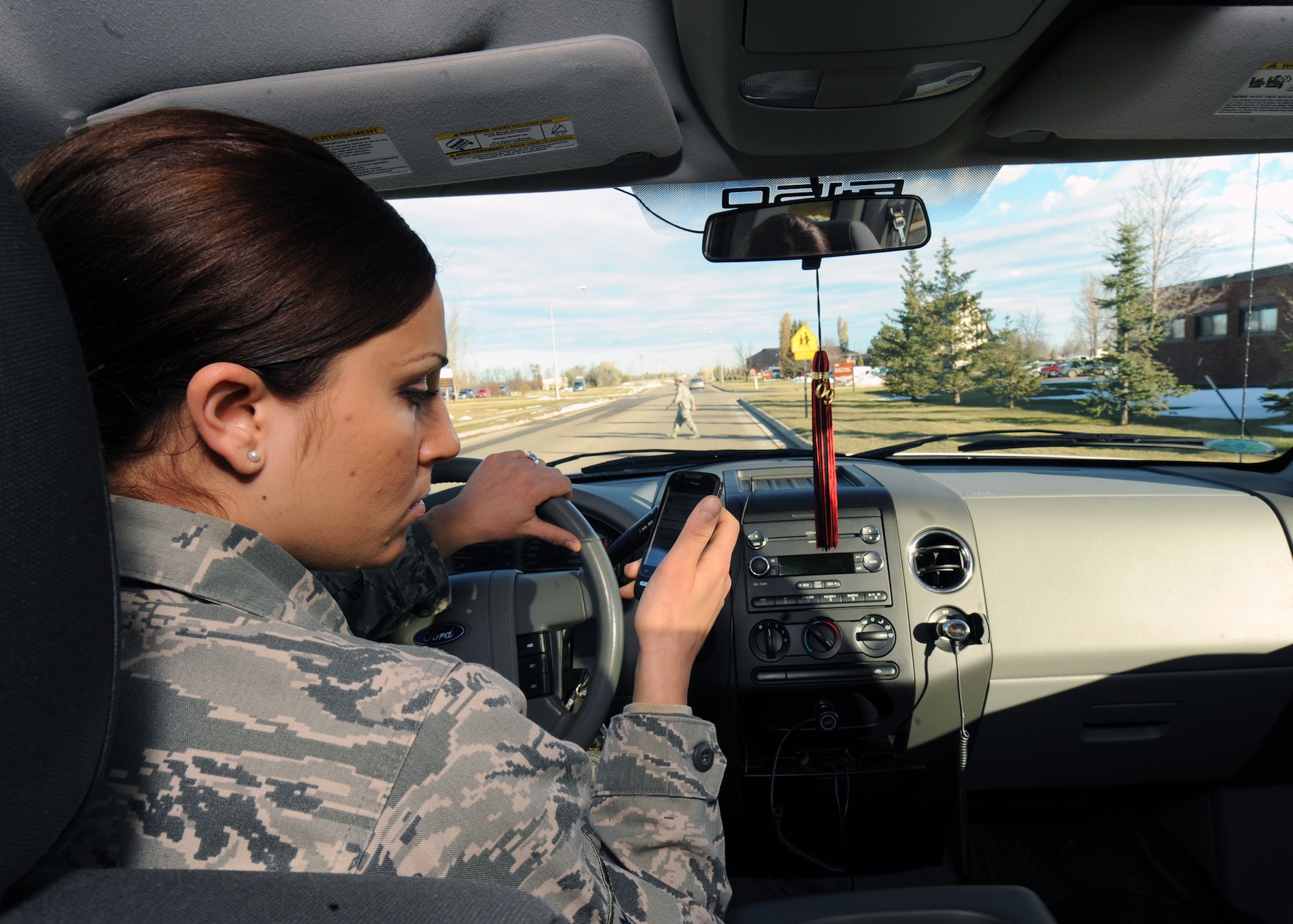 MINOT AIR FORCE BASE, N.D. -- Using a cell phone while driving a car has been proven to be dangerous. Airman 1st Class Jessica McConnell, Minot AFB Public Affairs staff writer, demonstrates the hazards associated with texting while driving as a young Airman uses a crosswalk. (U.S. Air Force photo by Staff Sgt. Keith Ballard)