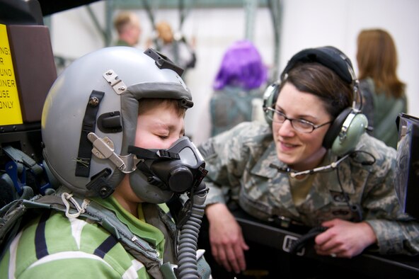 Keegan Hall, 12, breathes through an oxygen mask, Oct. 29, 2010, in the F-22 Raptor egress procedure trainer at Joint Base Elmendorf-Richardson with the help of Tech. Sgt. Chelsea De La Fuente. Sergeant DeLa Fuente is with the Aircrew Flight Equipment Flight, 3rd Operations Support Squadron. (U.S. Air Force photo/David Bedard)
