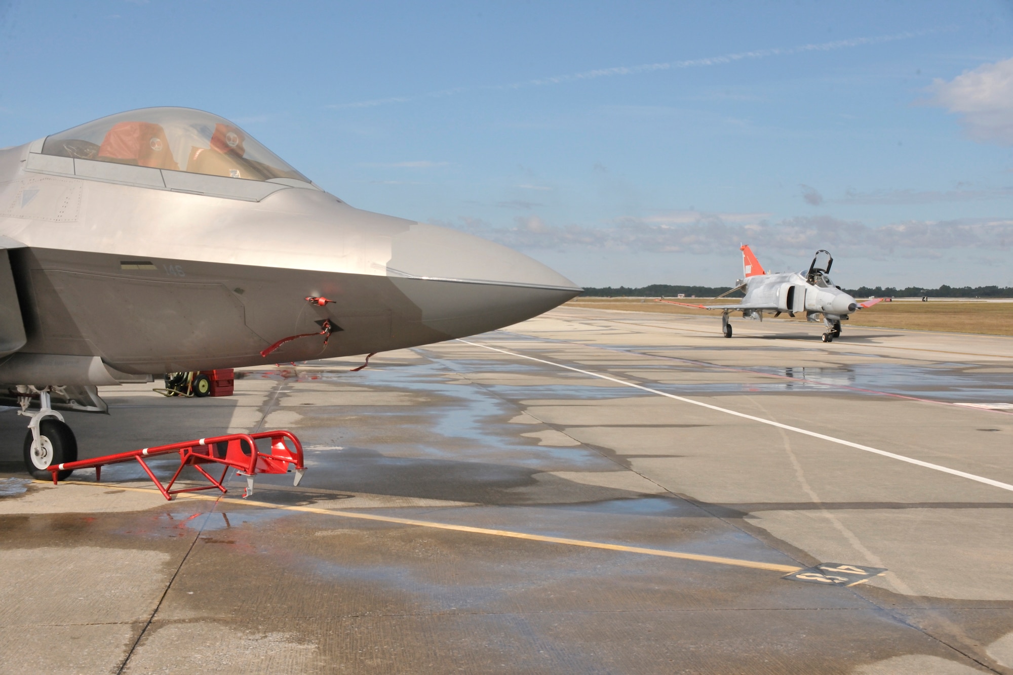 A QF-4 from the 82nd Aerial Targets Squadron at Tyndall AFB, Fla. taxies by an F-22 from Joint Base Elmendorf-Richardson.  The QF-4 is supersonic and is a reusable full-scale target drone modified from the F-4 Phantom. The QF-4 provides a realistic full-scale target for air-to-air weapons system evaluation, development and testing.  WSEP’s full mission includes loading missiles, flying with and firing missiles and hitting targets.  (U.S. Air Force photo/Technical Sgt. John Hoffman)