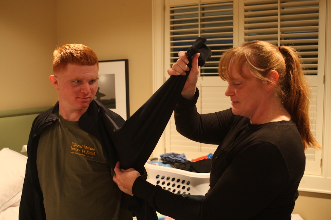 Yevon McClelland, a current tenant of the Fisher House, assists her son, Lance Cpl. Joshua Keel, now with Wounded Warrior Battalion - East, in putting on a jacket in their room of the Fisher House, Nov. 8. Due to his injury, Keel's mother is staying at the Fisher House with him to help him with everyday activities that he is now unable to do himself.