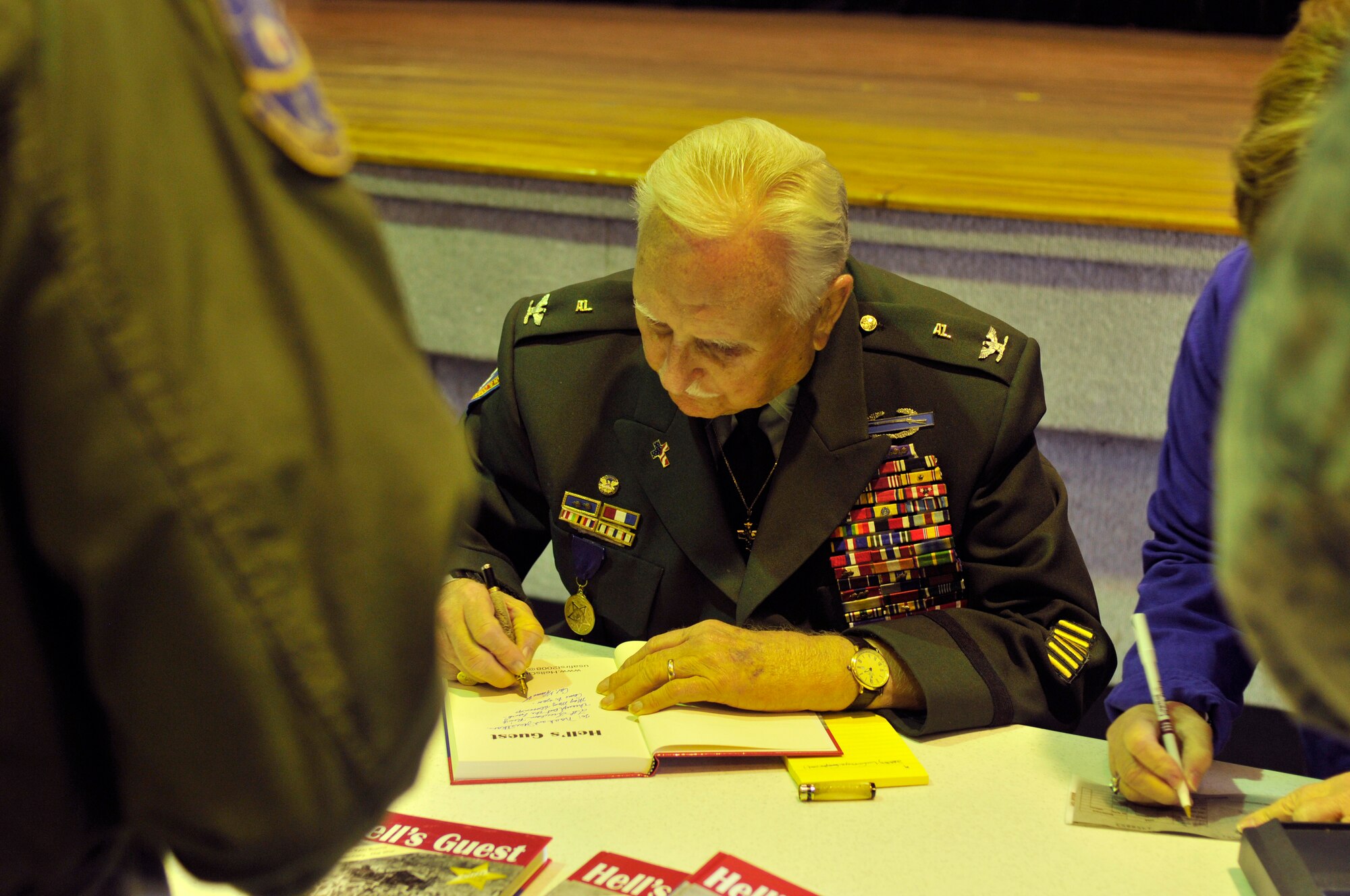 PATRICK AIR FORCE BASE, Fla. ? Colonel Glenn Frazier, recipient of the Medal of Freedom, the Bronze Star, four Purple Hearts and many, many more awards and recognitions than most, signs his book, ?Hell?s Guest,? for awaiting Reserve Airmen. Colonel Frazier was invited to speak at the 920th Rescue Wing here about his grueling experiences as a Prisoner of War during the Bataan Death March at the start of World War II.  Details of the march were lived by men like Colonel Frazier. The men were surrounded by death; beheading, throat-cutting and shooting were common causes of death but deliberate starvation, dehydration, stabbing with bayonet and rifle-butt beatings were also prevalent during the week-long continual march. The 60 mile trek would be like walking from here to Orlando, Fla., in the middle of sweltering August. (U.S. Air Force photo/Staff Sgt. Leslie Kraushaar)