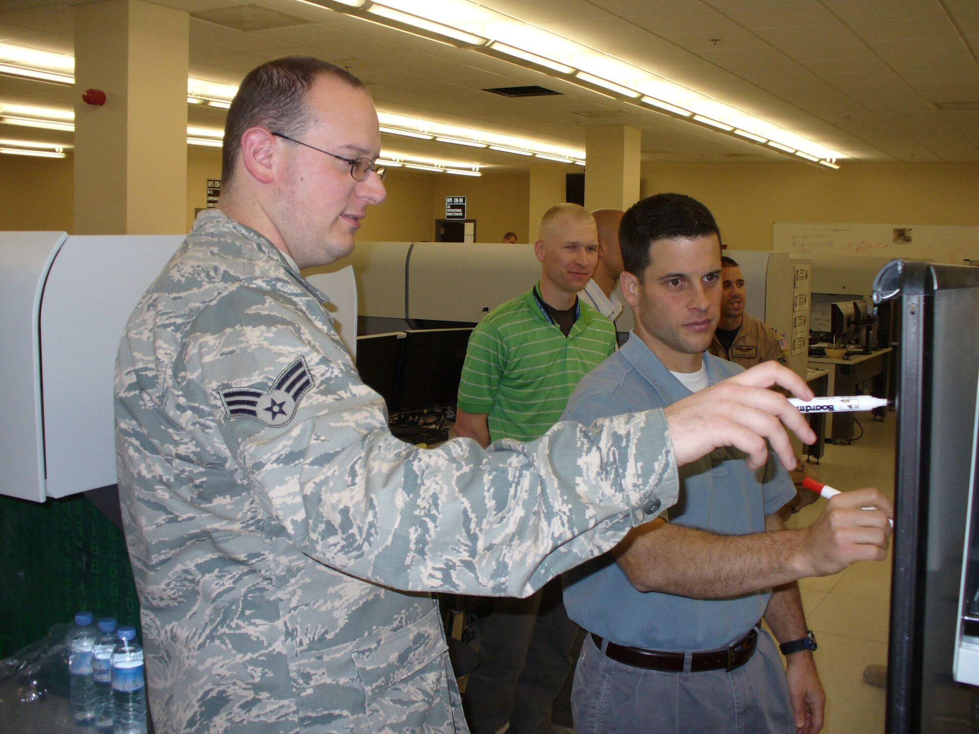 Senior Airman Josh Miller, Air Forces Central/Air Force Forces A6 Division software engineer, discusses how to combine intelligence, surveillance and reconnaissance planning capabilities with Stephen Harrison and David Greeley in a combined air operations center in an area of responsibility in fall 2009. Mr. Harrison and Mr. Greeley are MITRE software developers and members of the Airspace Mission Planning Division's Advanced Development Team. (Courtesy photo) 

