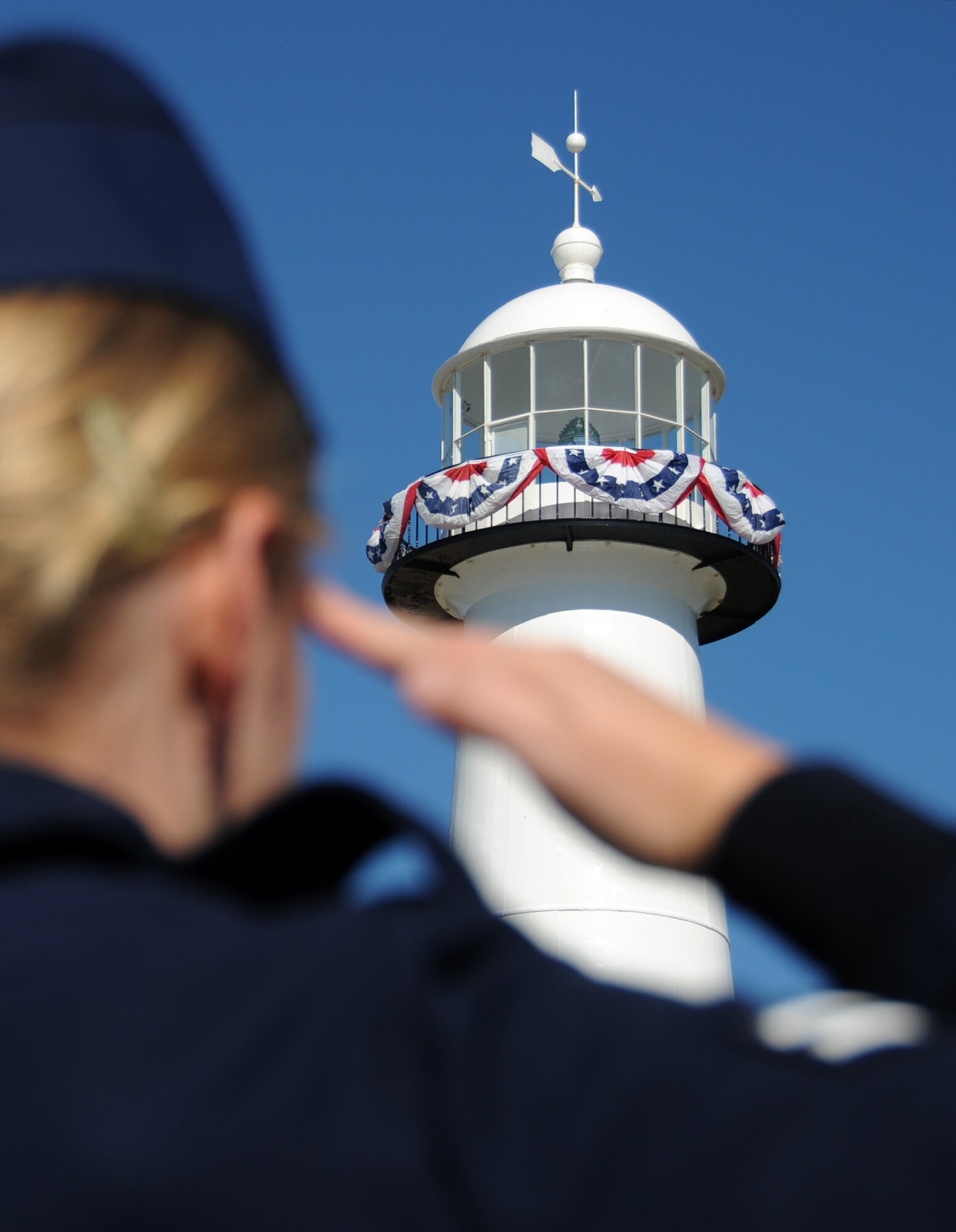 An Airman renders a salute in front of the Biloxi Lighthouse Monday. The Biloxi landmark is draped in red, white and blue bunting and four candles are burning in
each of the four windows as a Veterans Day tribute by Staff Sgt. Brian Margavich, 333rd Training Squadron. Sergeant Margavich, the city’s volunteer lighthouse
keeper, got the idea from the Chris Lights project, in which single tapers burn in house windows year-round to remember deployed military personnel. He burned a candle in the window while his wife, Staff Sgt. Amanda Margavich, 81st Force Support  squadron, was deployed last year. After a discussion with Trisha Meagher, wife of Staff Sgt. Frank Meagher, a deployed member of his squadron, Sergeant Margavich decided to use the candles as a tribute to all deployed troops. Victoria Nores, a friend he met through the Ocean Springs Relay for Life, assisted him with the decorations.  (U.S. Air Force photo by Kemberly Groue)