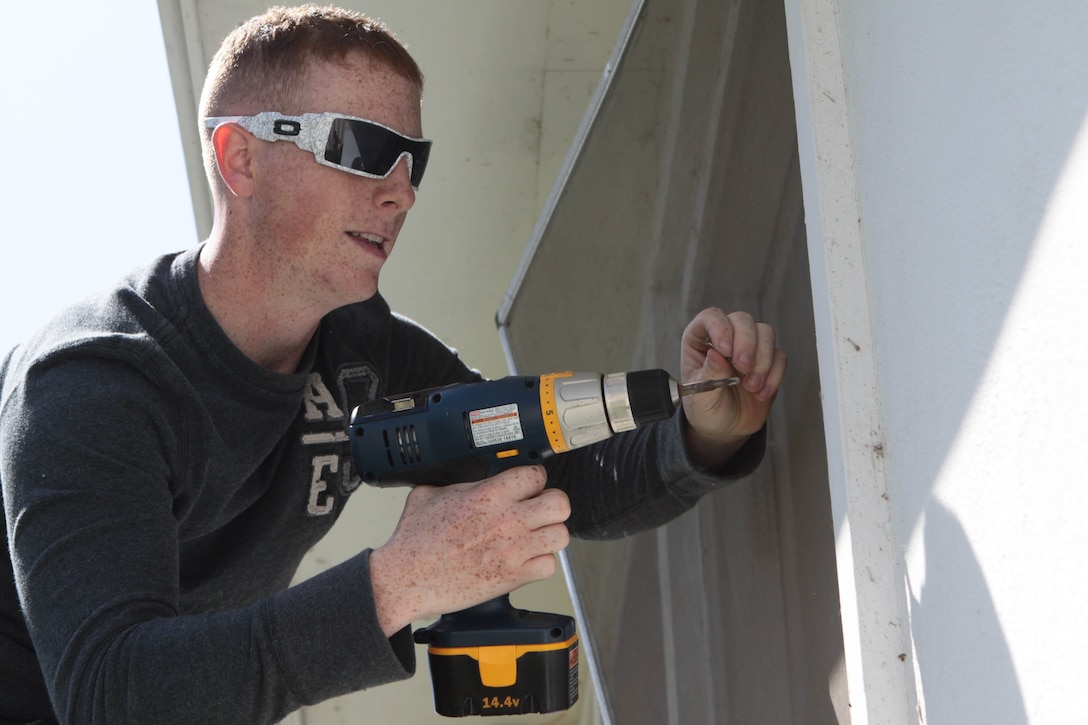 Lance Cpl. Nicholas Day unscrews a screen to clean the window at the Navy Marine Corps Relief Society Thrift Store on Camp Pendleton May 9. The Mairnes work together to clean the windows and window screens of the store help its ventilation during the summer season. Day is a military policeman with Military Police Compant, Security Battalion.