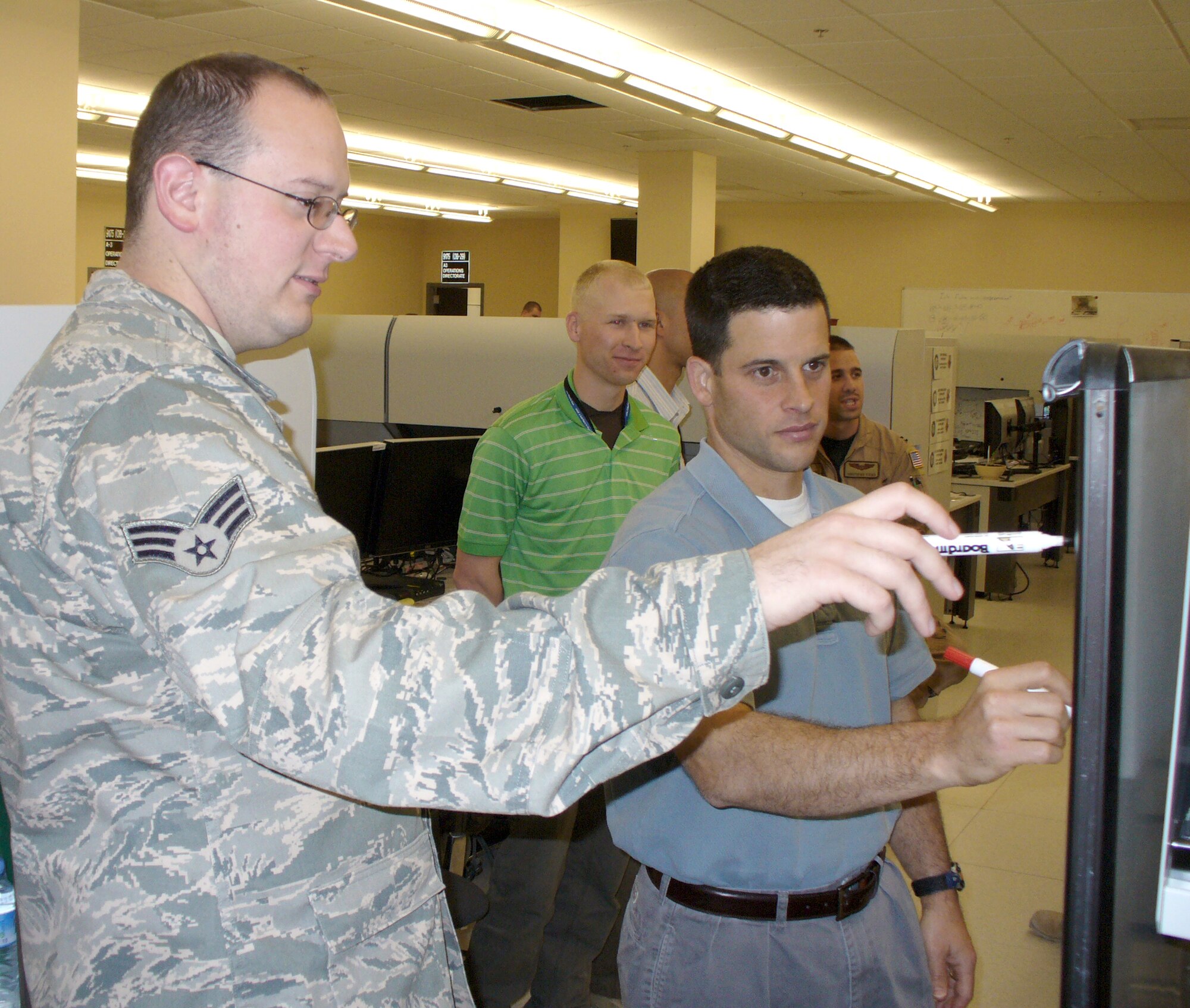 Senior Airman Josh Miller discusses how to combine intelligence, surveillance and reconnaissance planning capabilities with Stephen Harrison and David Greeley in a combined air operations center in an area of responsibility in fall 2009. Mr. Harrison and Mr. Greeley are MITRE software developers and members of the Airspace Mission Planning Division's advanced development team. Airman Miller is an Air Forces Central software engineer. (Courtesy photo)